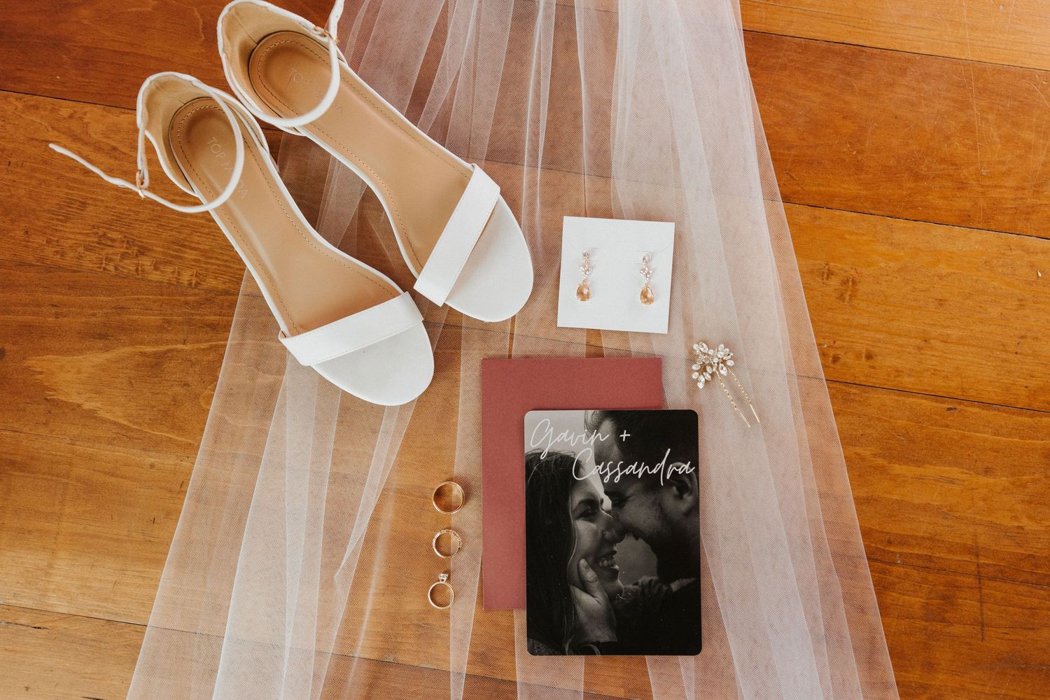 Wedding details featuring white shoes, veil and photo cards on wooden floor.