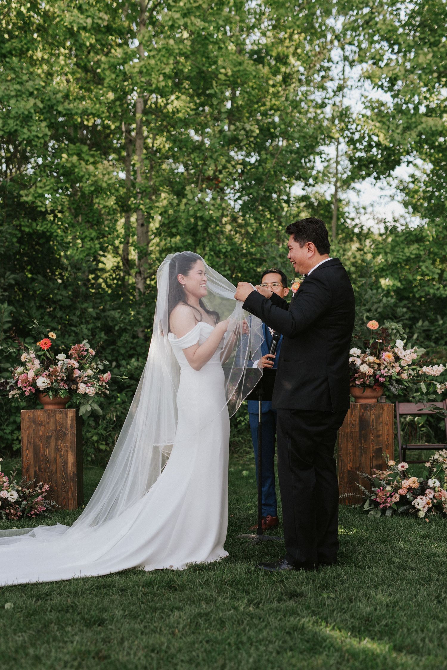 Couple exchanges vows in garden setting with wooden arch and pink floral arrangements.