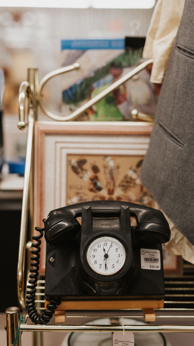 Vintage black rotary telephone with built-in clock displayed on shelf.
