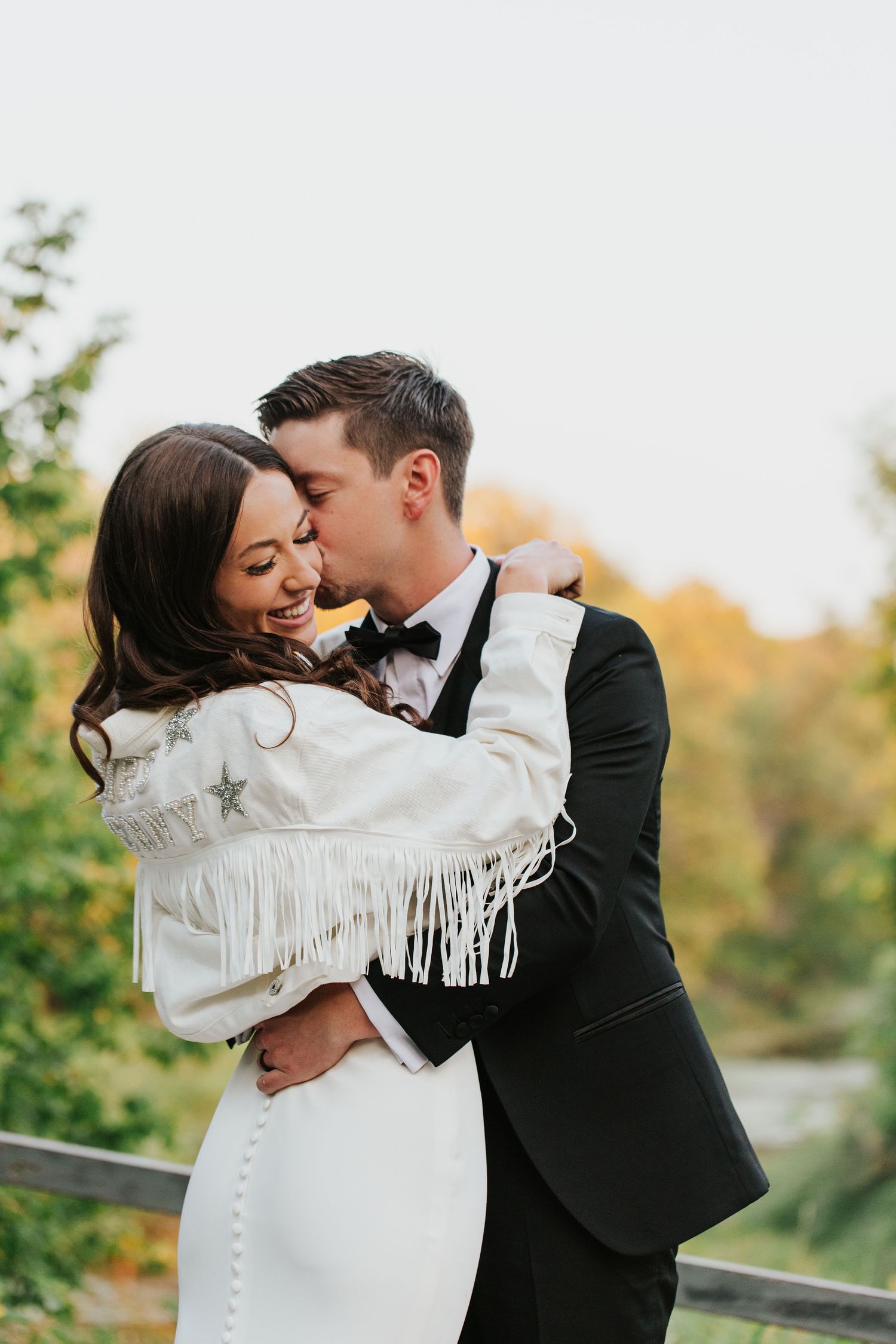 Couple embracing while wearing a white fringe jacket and formal attire.