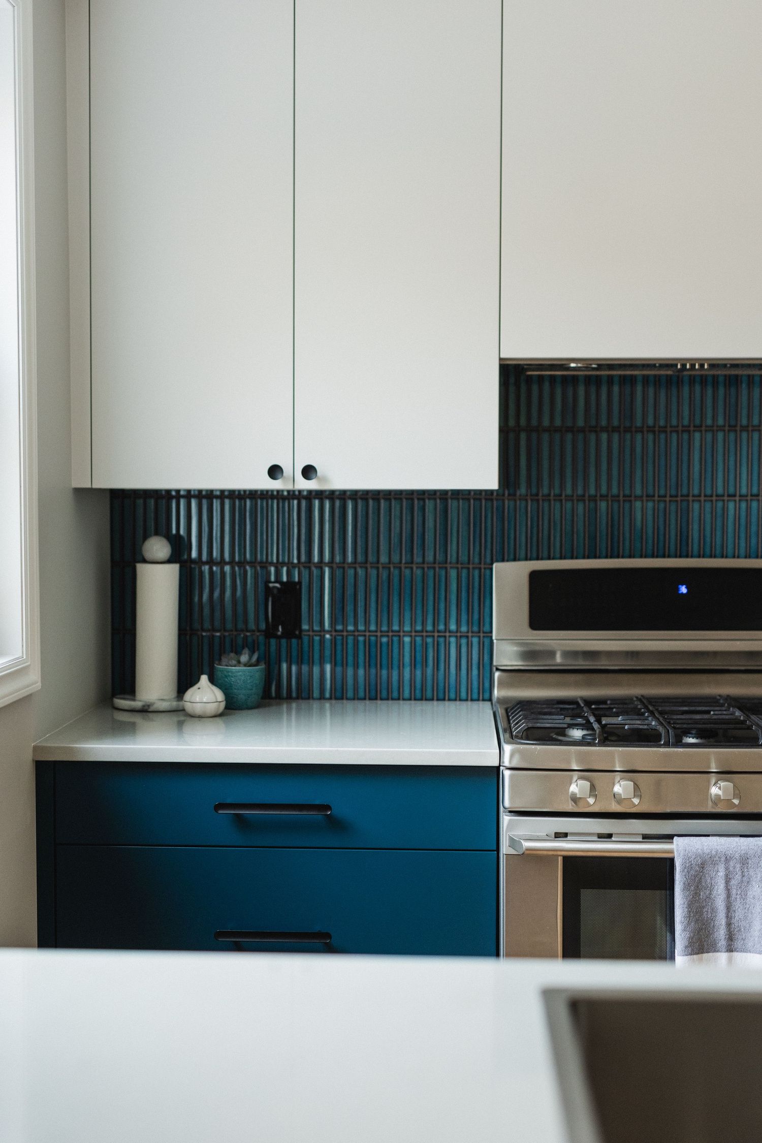 Modern kitchen with white cabinets, blue backsplash tile, and stainless steel appliances.