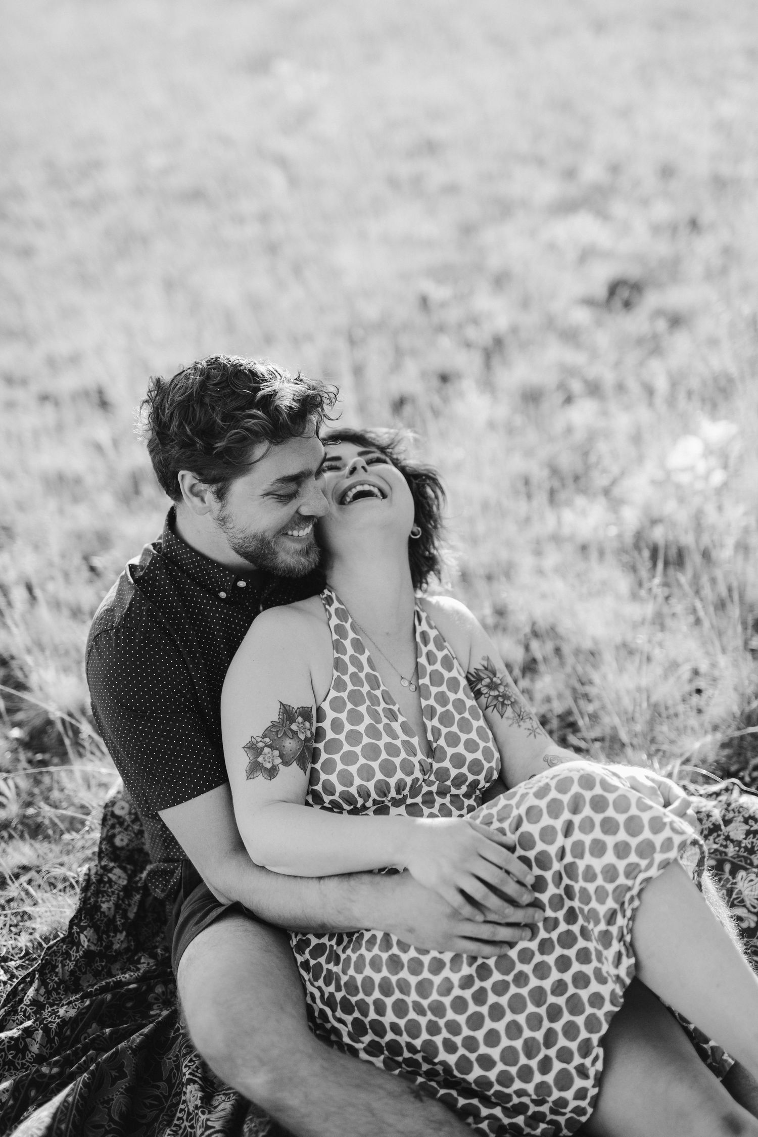 A black and white photo of a couple laying together in a grassy field.