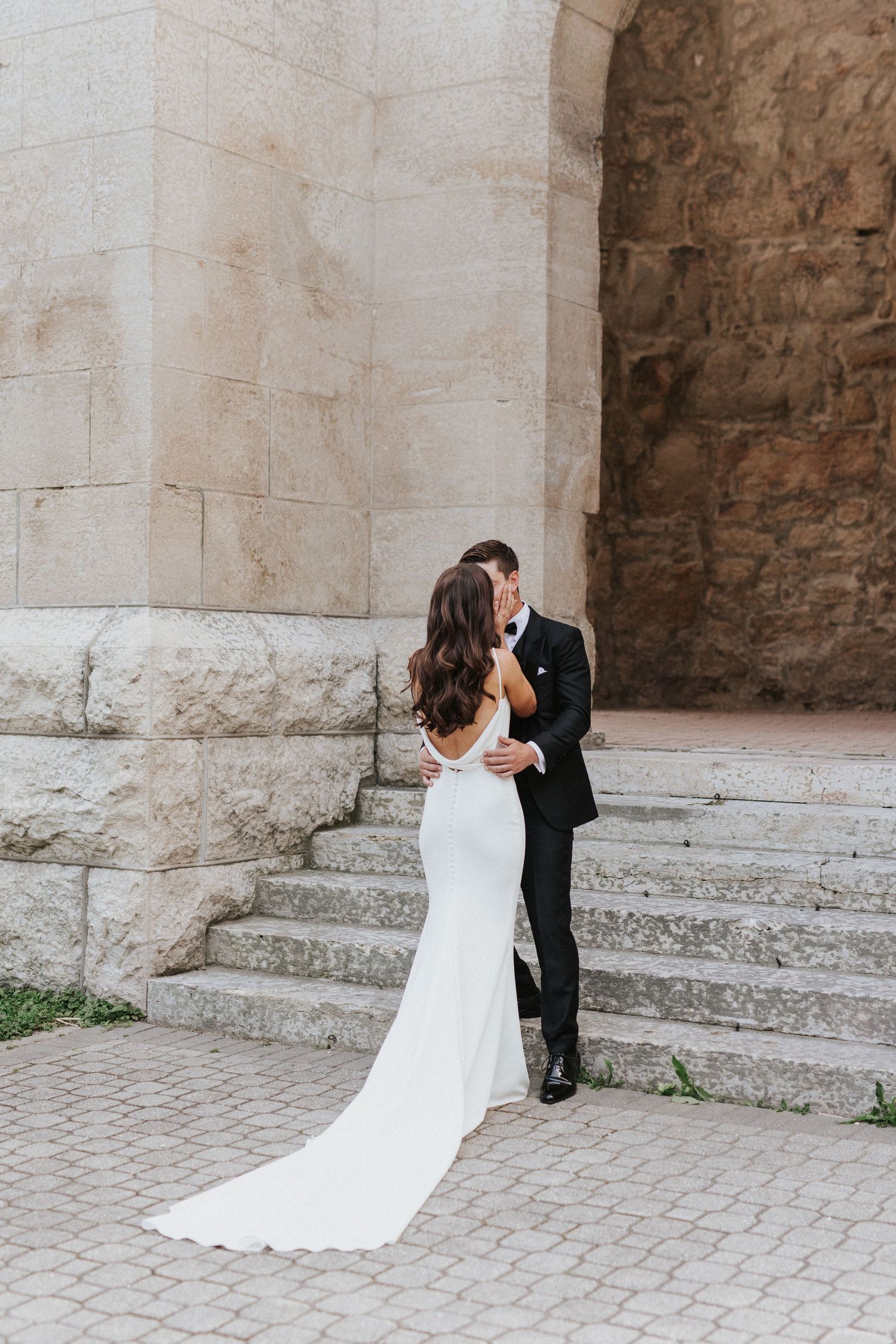 Romantic wedding portrait of couple embracing under stone archway on steps.