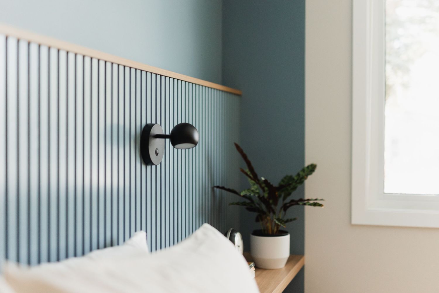 Blue accent wall with vertical wood paneling adds architectural interest to a modern bedroom space.
