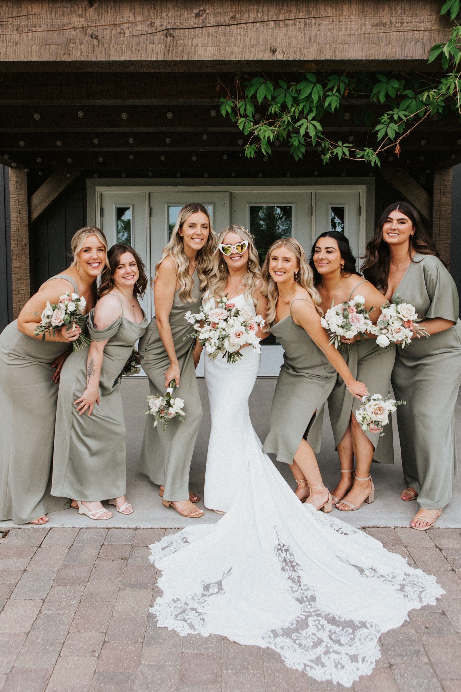 Bridal party in elegant gray dresses and white wedding gowns posing together outdoors.