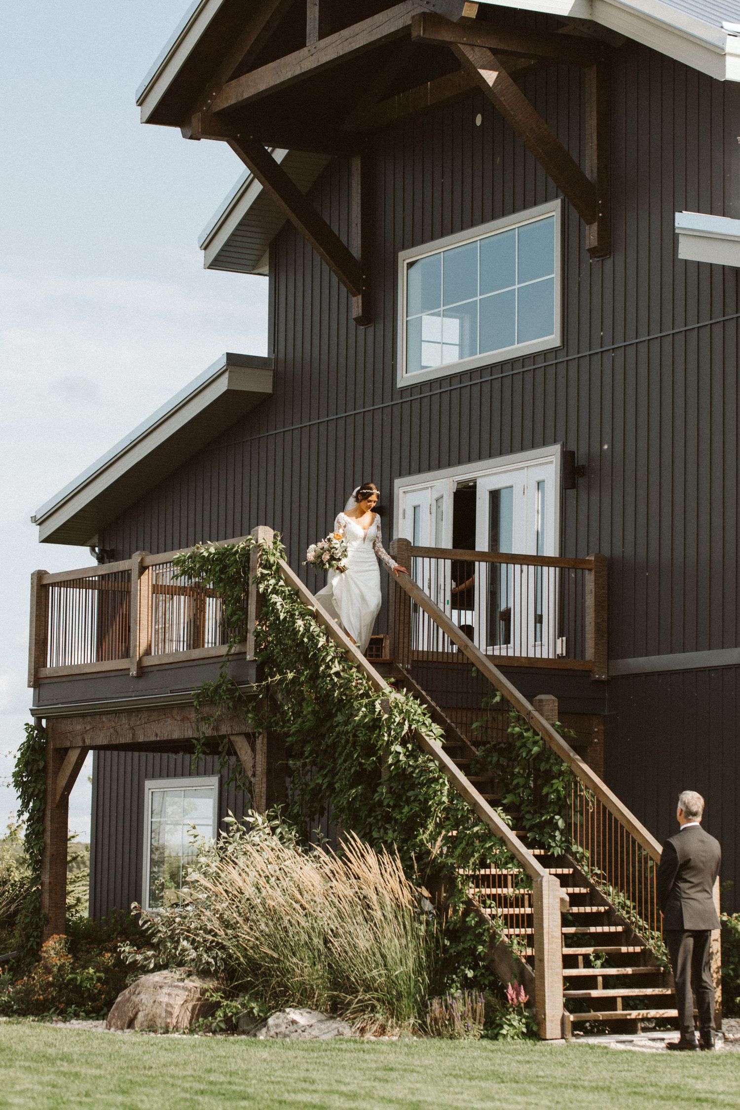 Modern dark barn-style wedding venue with wooden stairs and ornamental grasses.