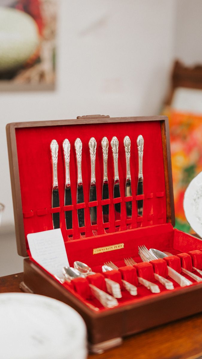 Vintage silverware set displayed in a brown case with red velvet lining.