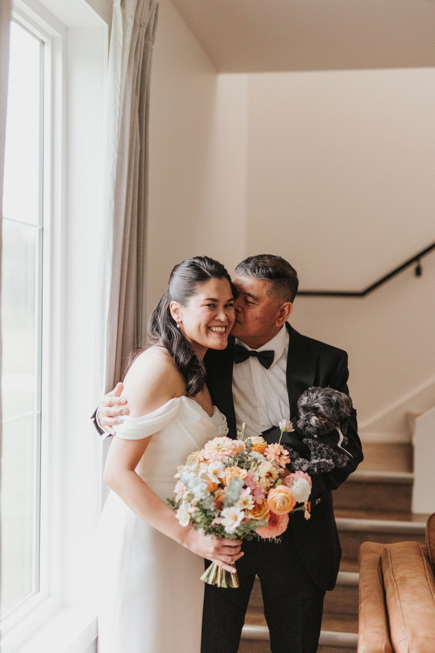 A romantic wedding moment by a window with the bride holding a beautiful peach and blush floral bouquet.