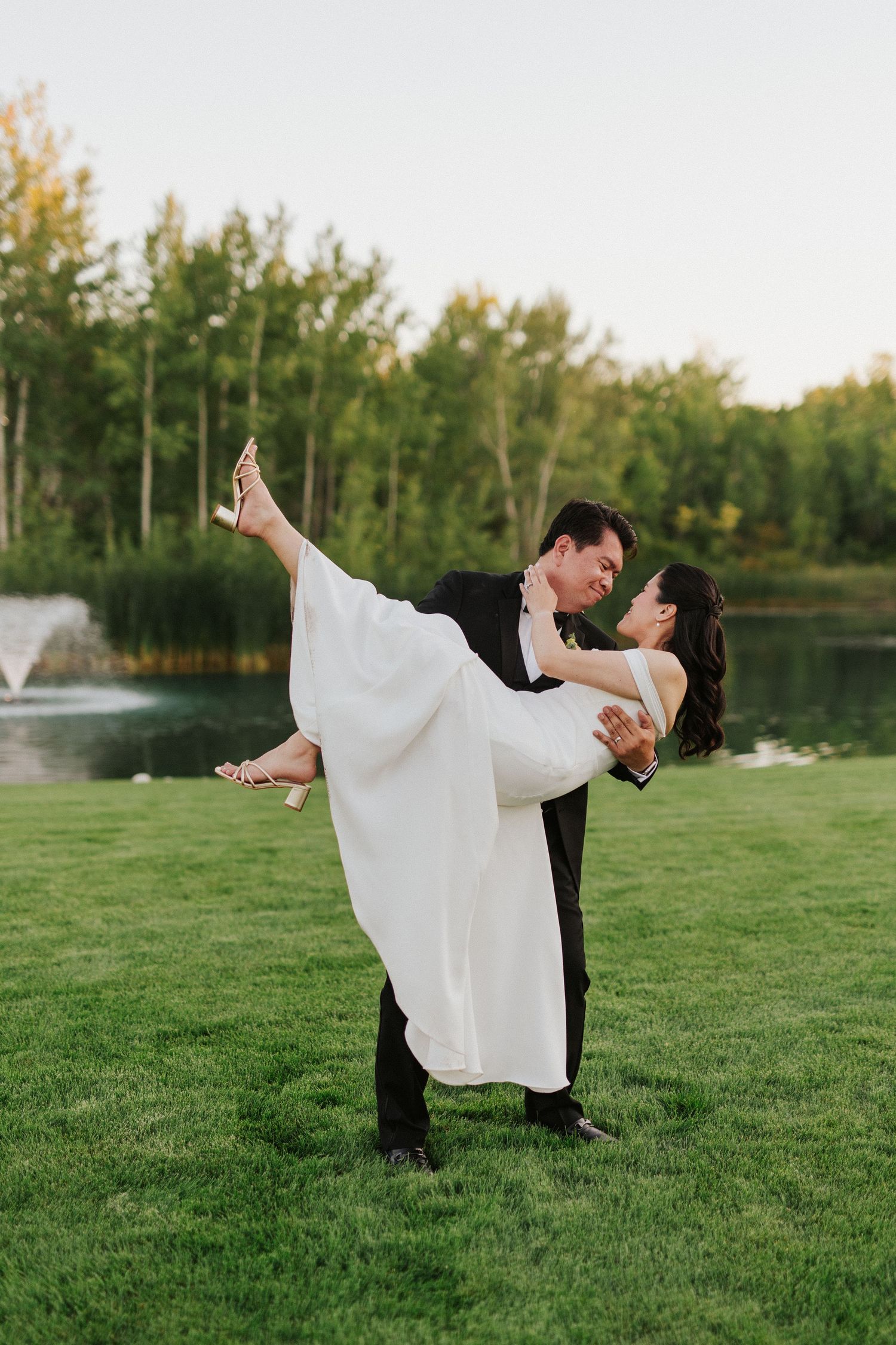 A couple dancing gracefully on a green lawn with trees in the background during golden hour.
