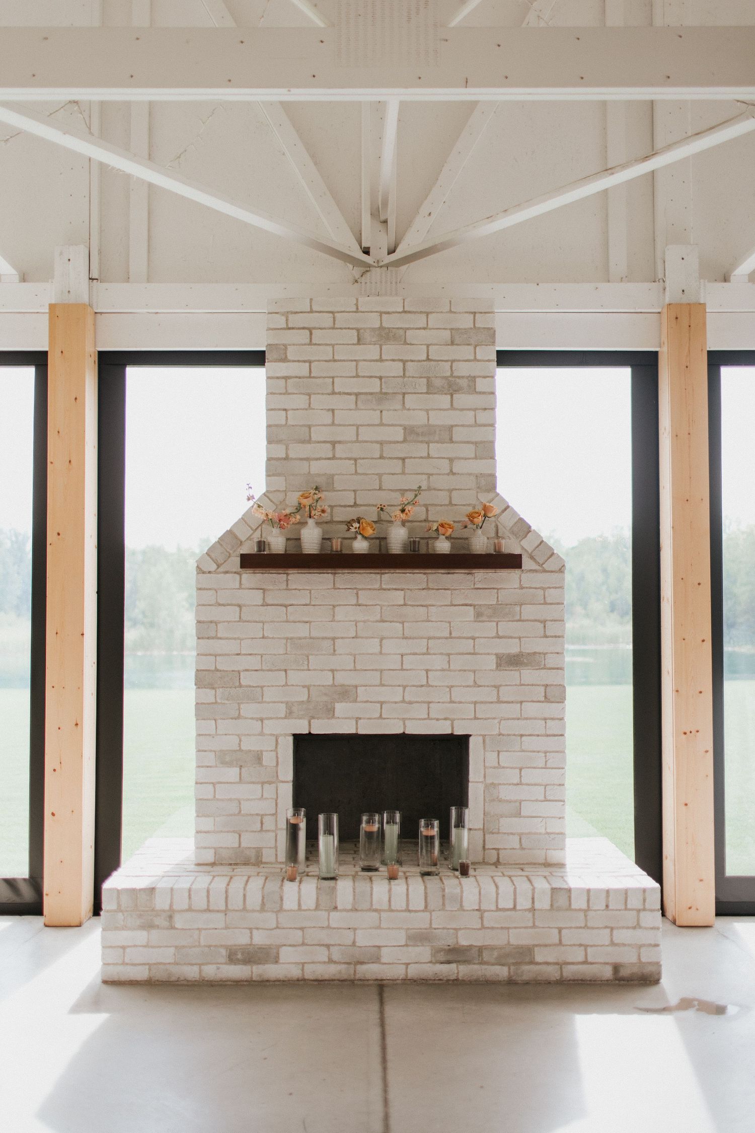 Modern white brick fireplace with exposed wooden beams in an elegant open concept room with large windows.