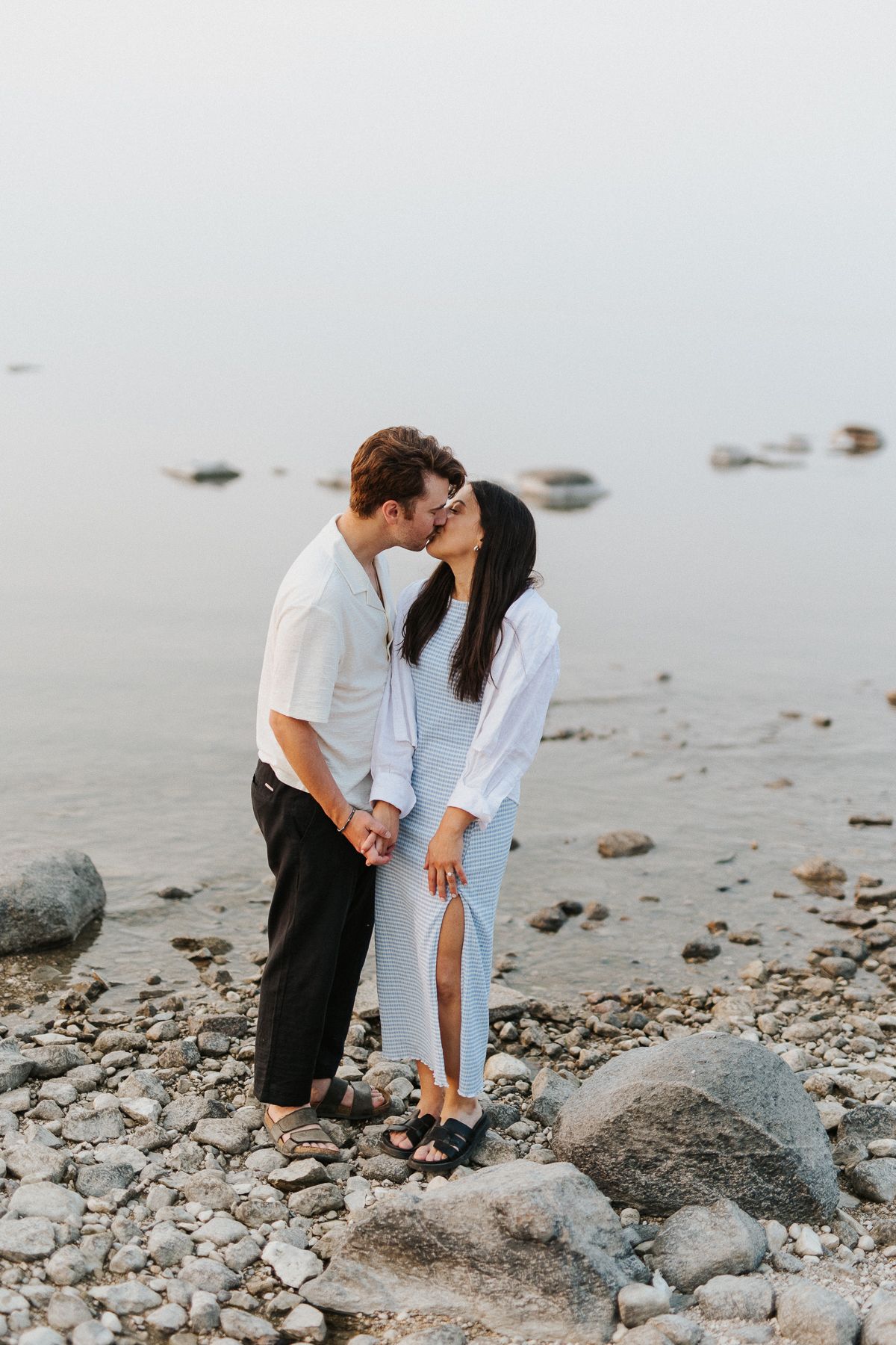 Intimate moment shared between couple sitting on rocky beach. Gimli, Manitoba, Canada