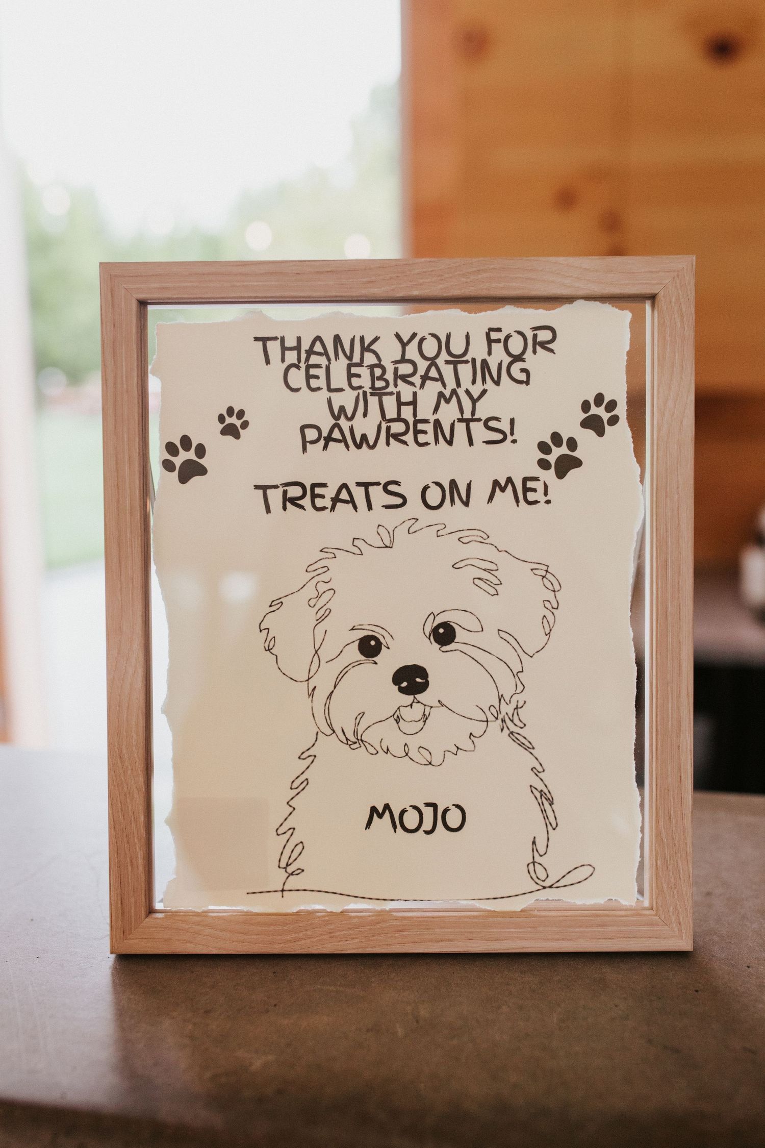 Hand-drawn sign featuring a cute puppy named Mojo thanking guests for celebrating with 'pawrents' and offering treats.