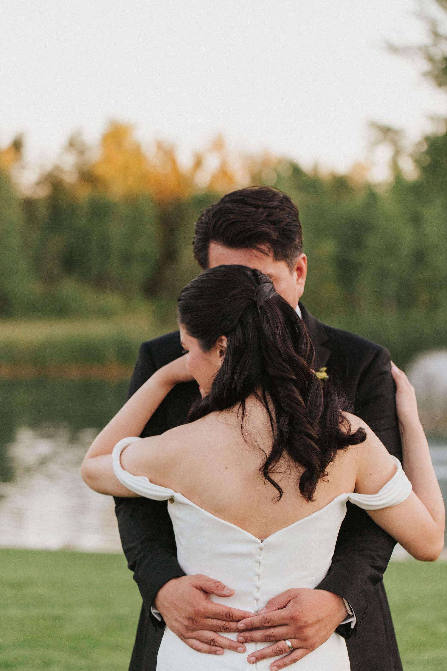 Romantic wedding photo of couple embracing by a lake at sunset.