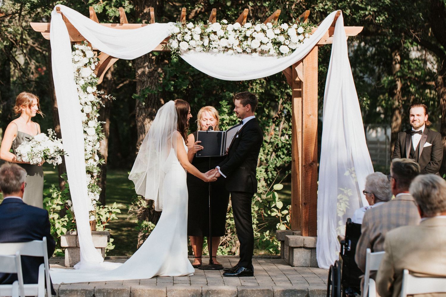 Outdoor garden wedding ceremony with white chairs and floral arch arrangements.