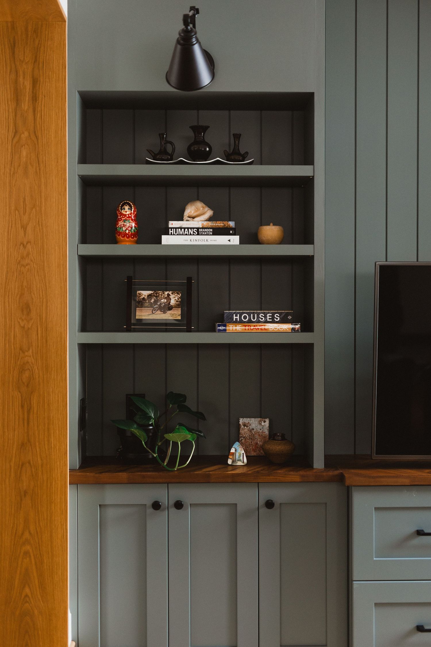 Custom built-in shelving unit in sage green displays books and decorative objects with wooden frame accents.