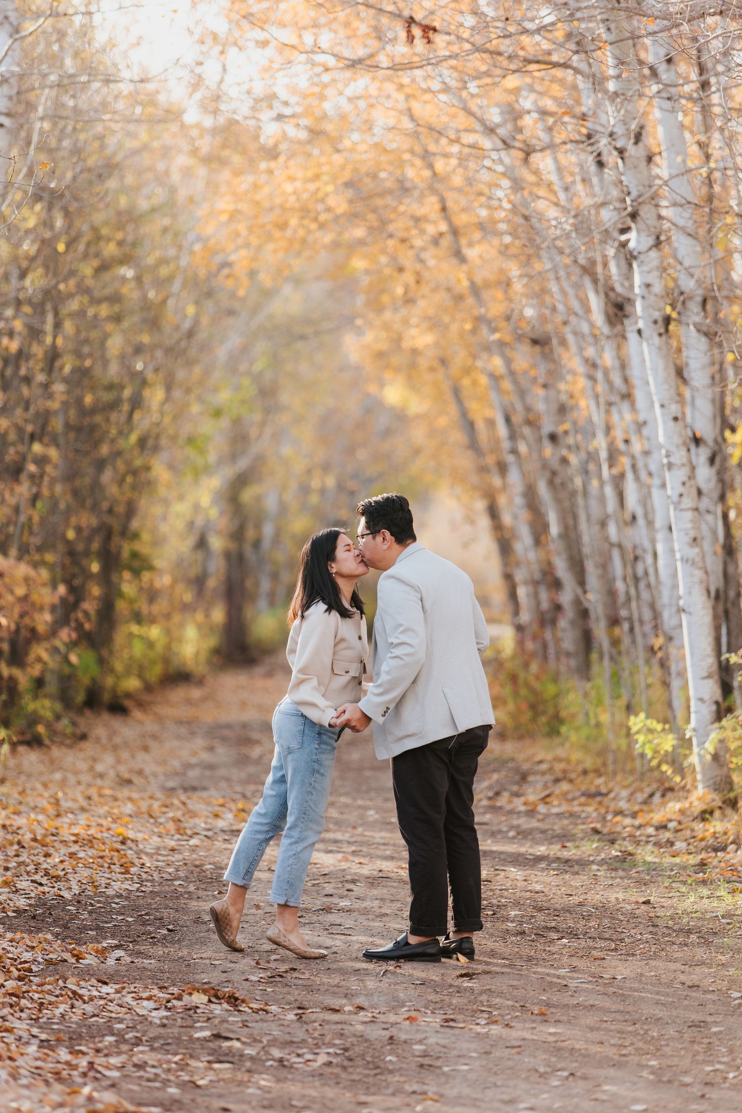 Playful couple shares romantic moments on tree-lined autumn path with golden foliage.