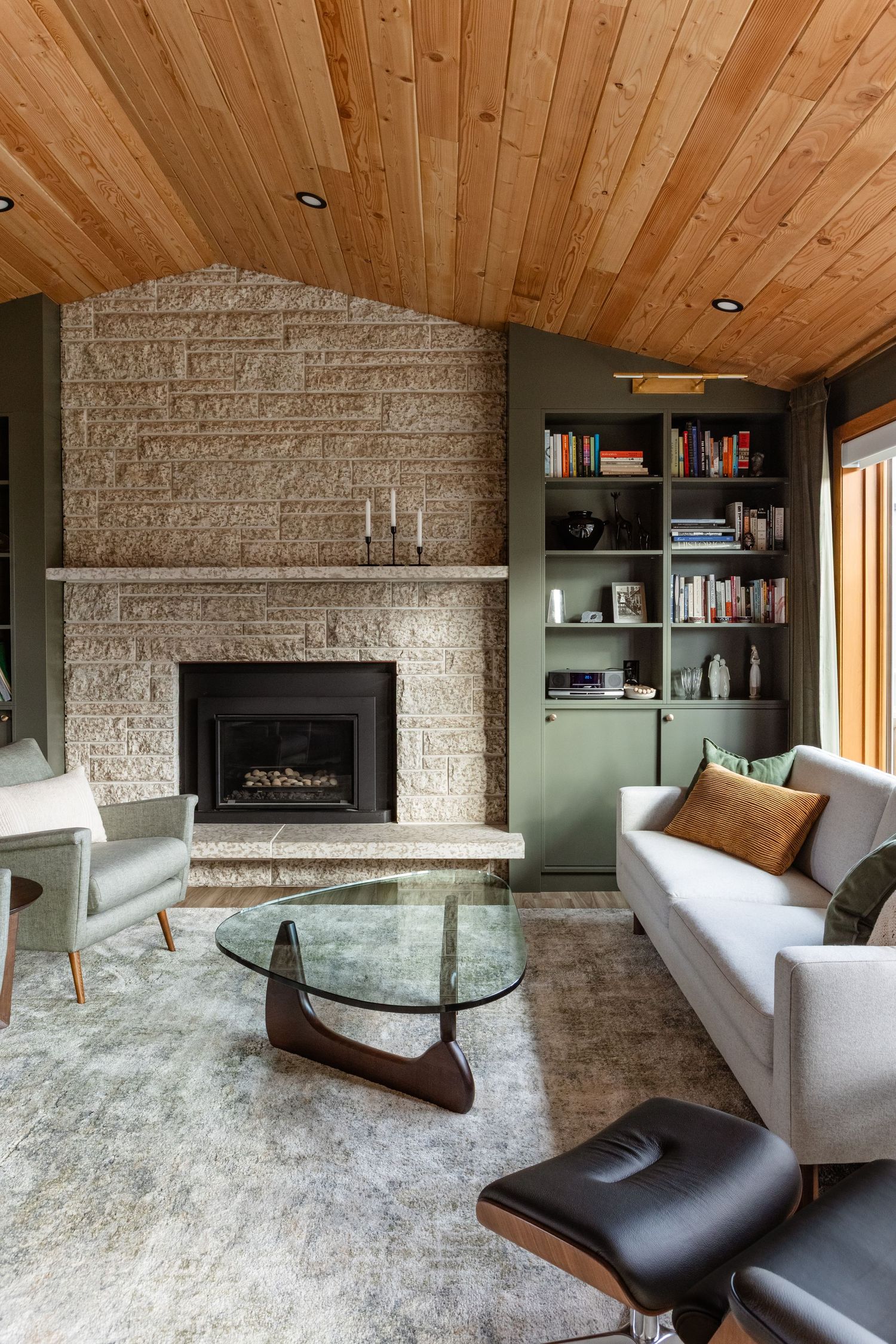 Cozy living room with stone fireplace, wooden ceiling, and modern furniture in sage green and gray tones.