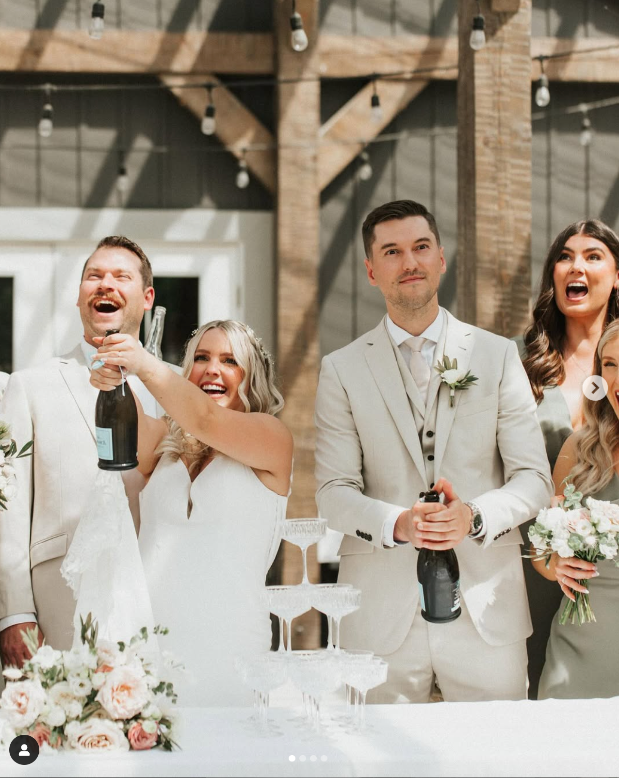 Wedding party laughing and celebrating with drinks in a rustic indoor venue.