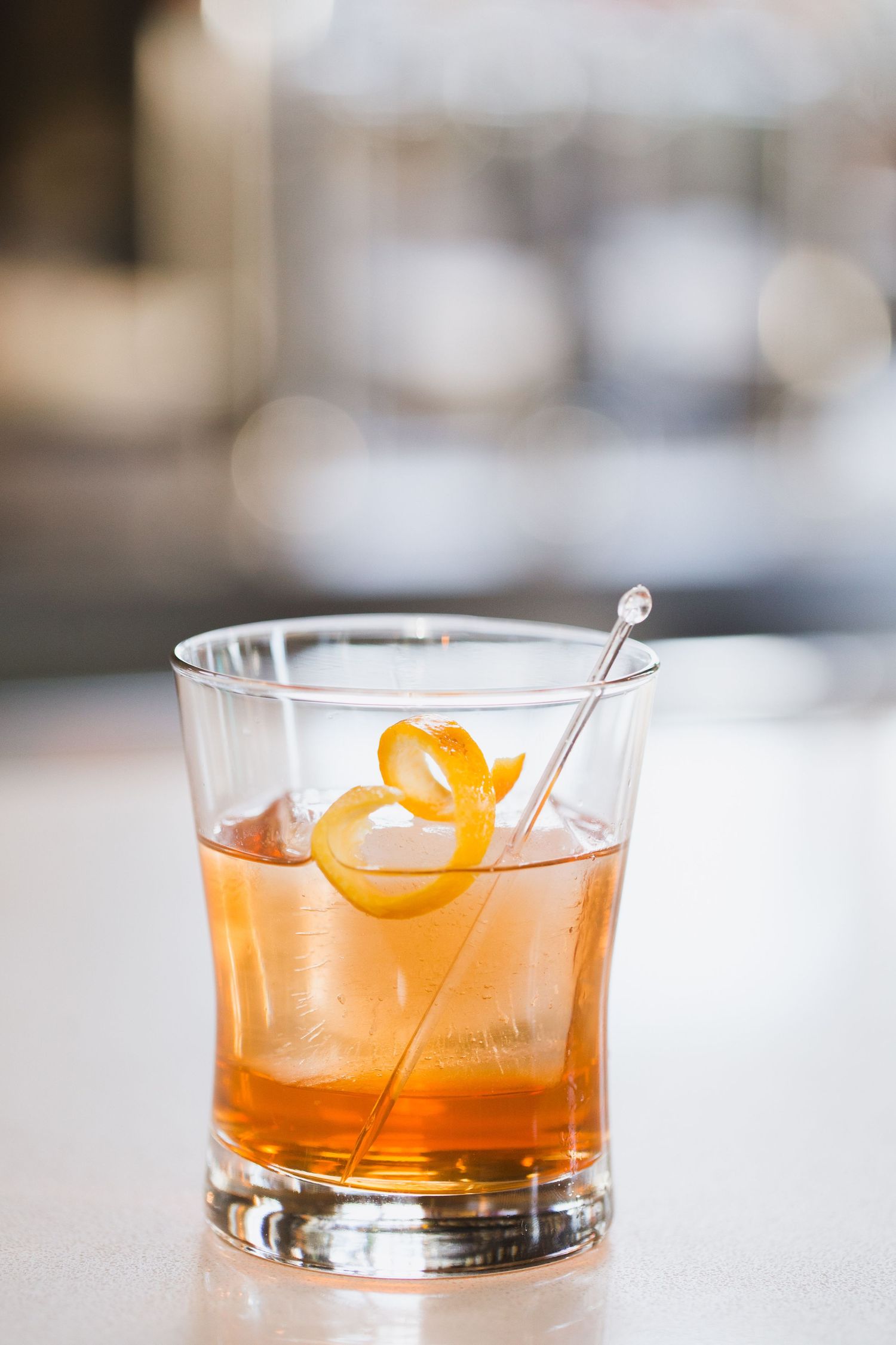 Craft cocktail with orange garnish in lowball glass with clear ice.