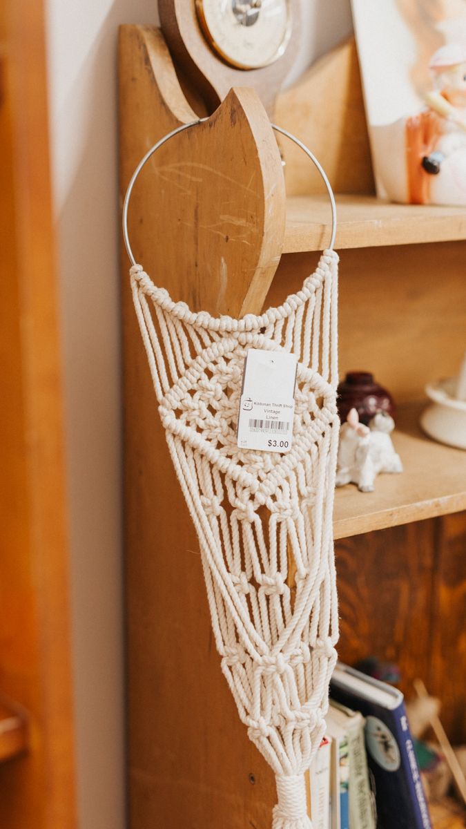 Handcrafted macrame wall hanging with intricate white knotwork pattern displayed on wooden surface.