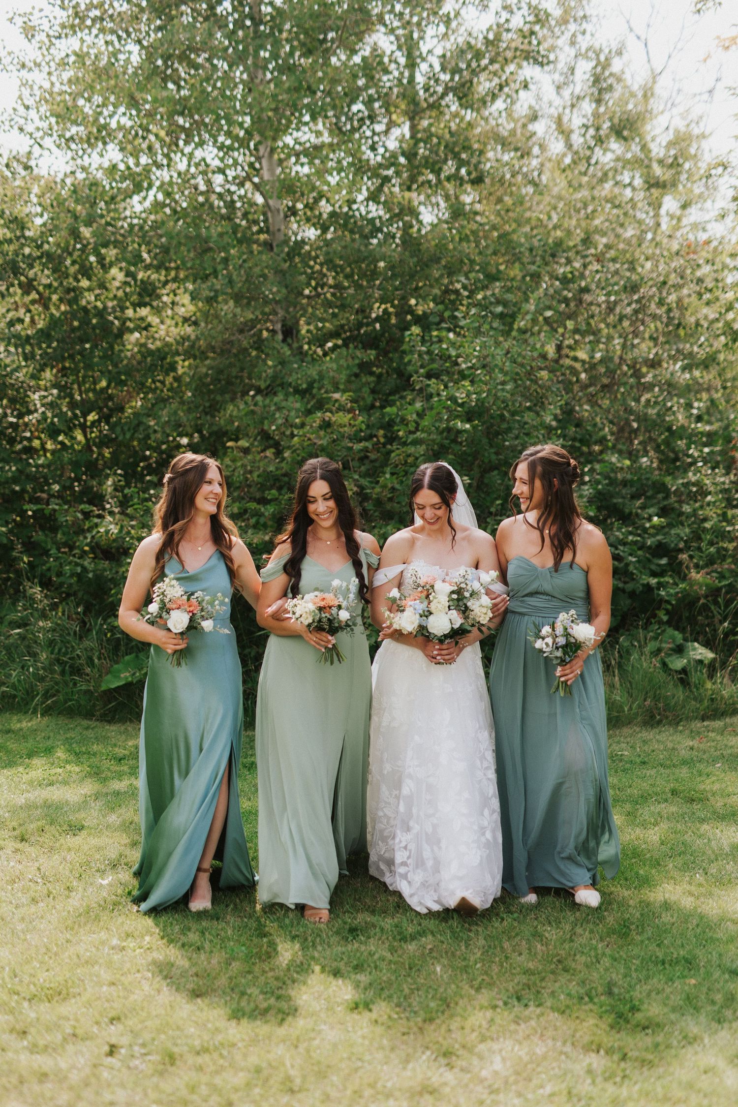 Wedding party in sage green dresses posing together on sunny lawn.