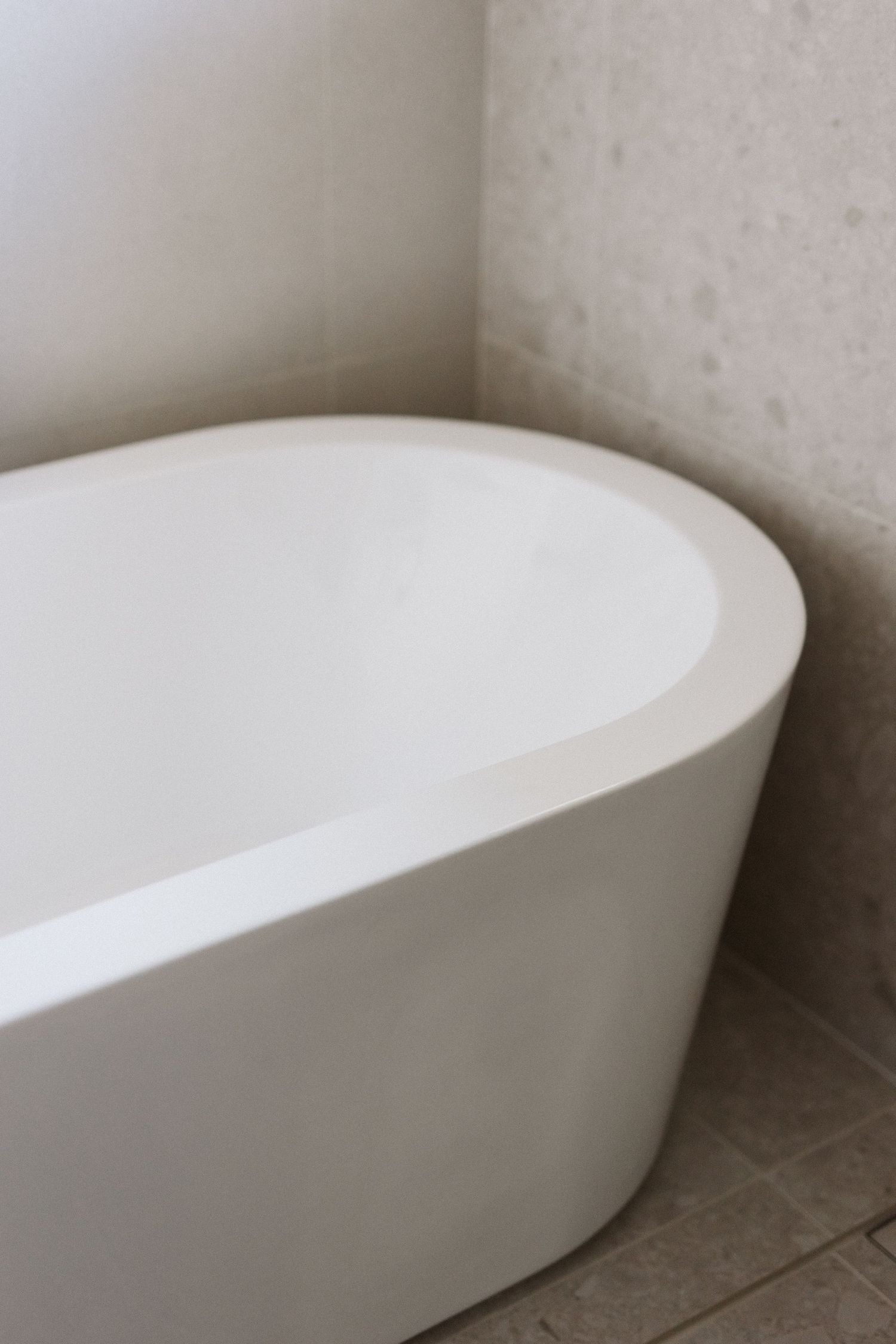 Minimalist white freestanding bathtub against light colored wall.