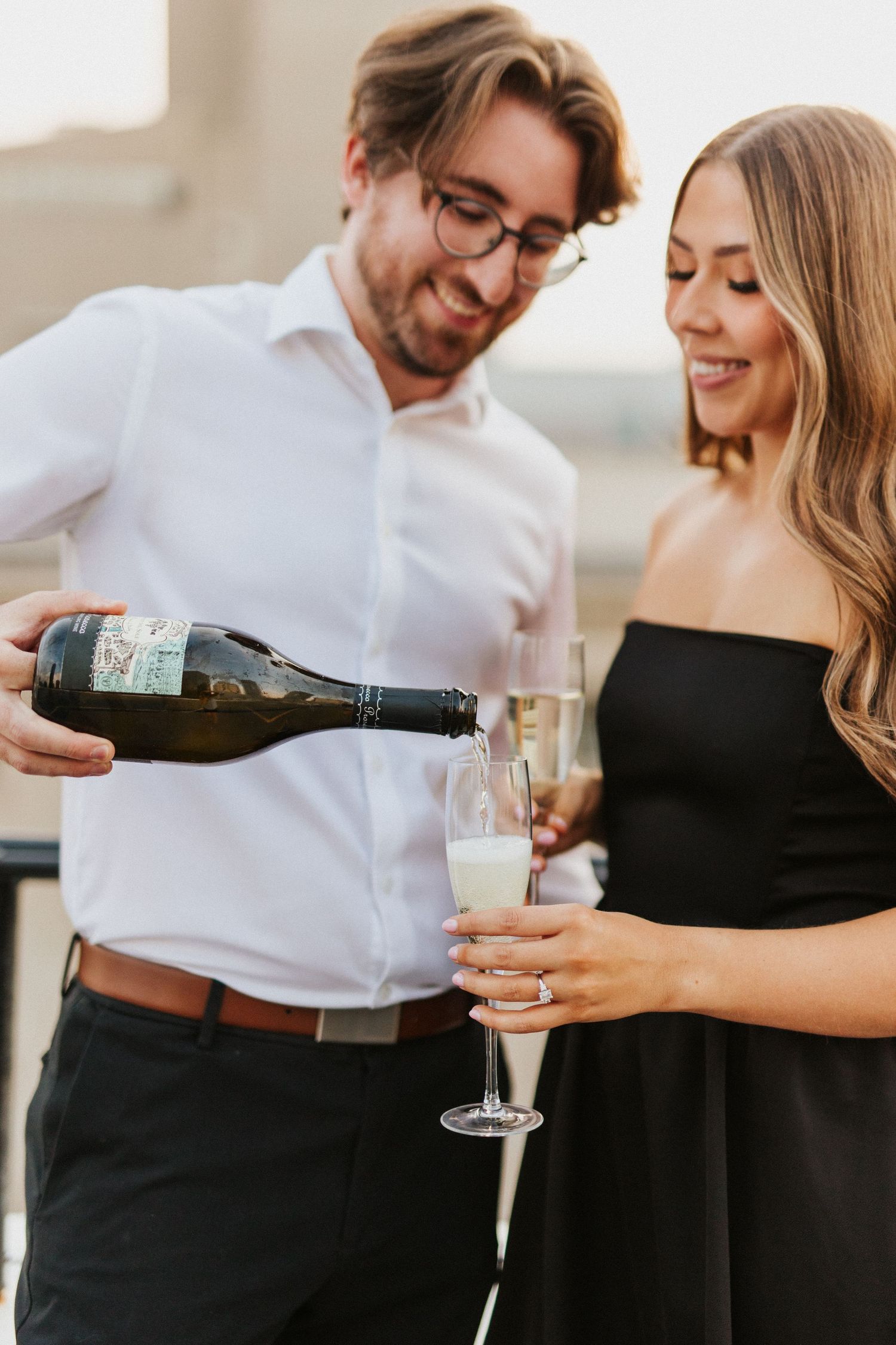A couple sharing wine and laughter in elegant black and white outfits.