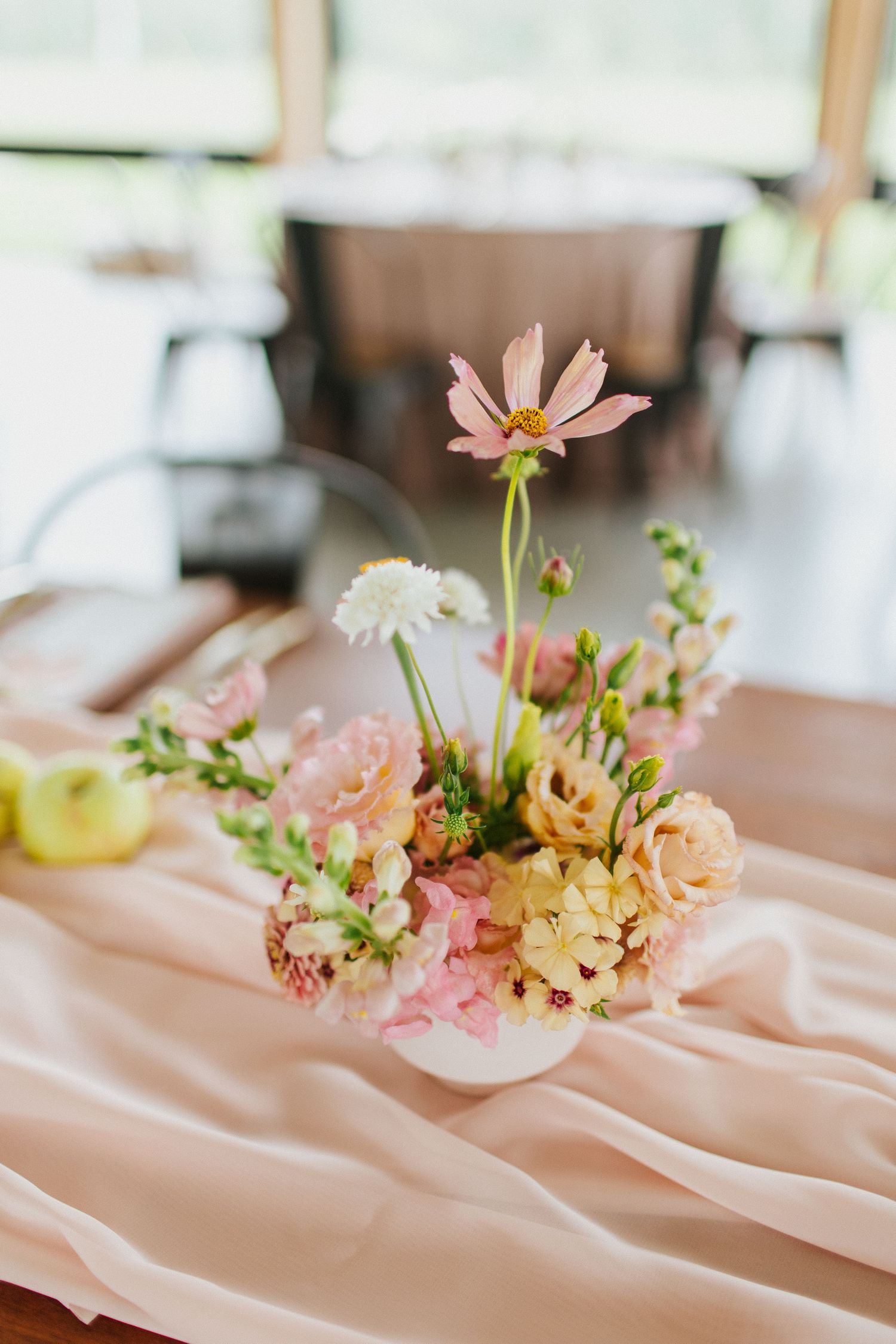 Delicate pink and peach floral arrangements with cosmos flowers displayed on soft blush fabric in a row.