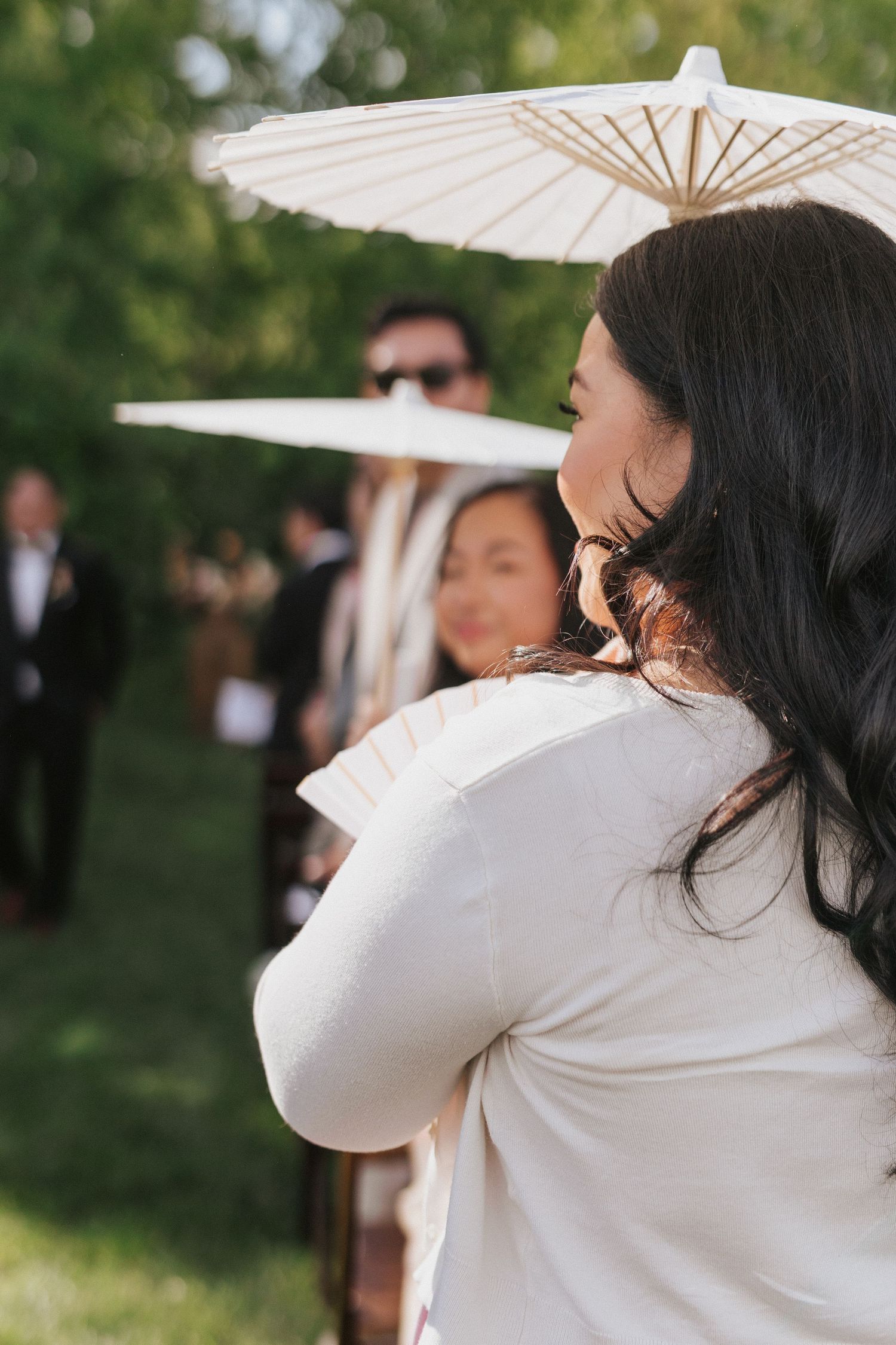 A person in white holds a delicate paper parasol against a green garden background.