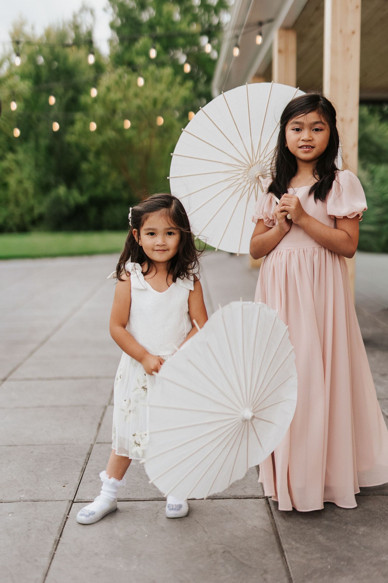 White paper parasols add elegance to a wedding party photo session on a concrete patio.