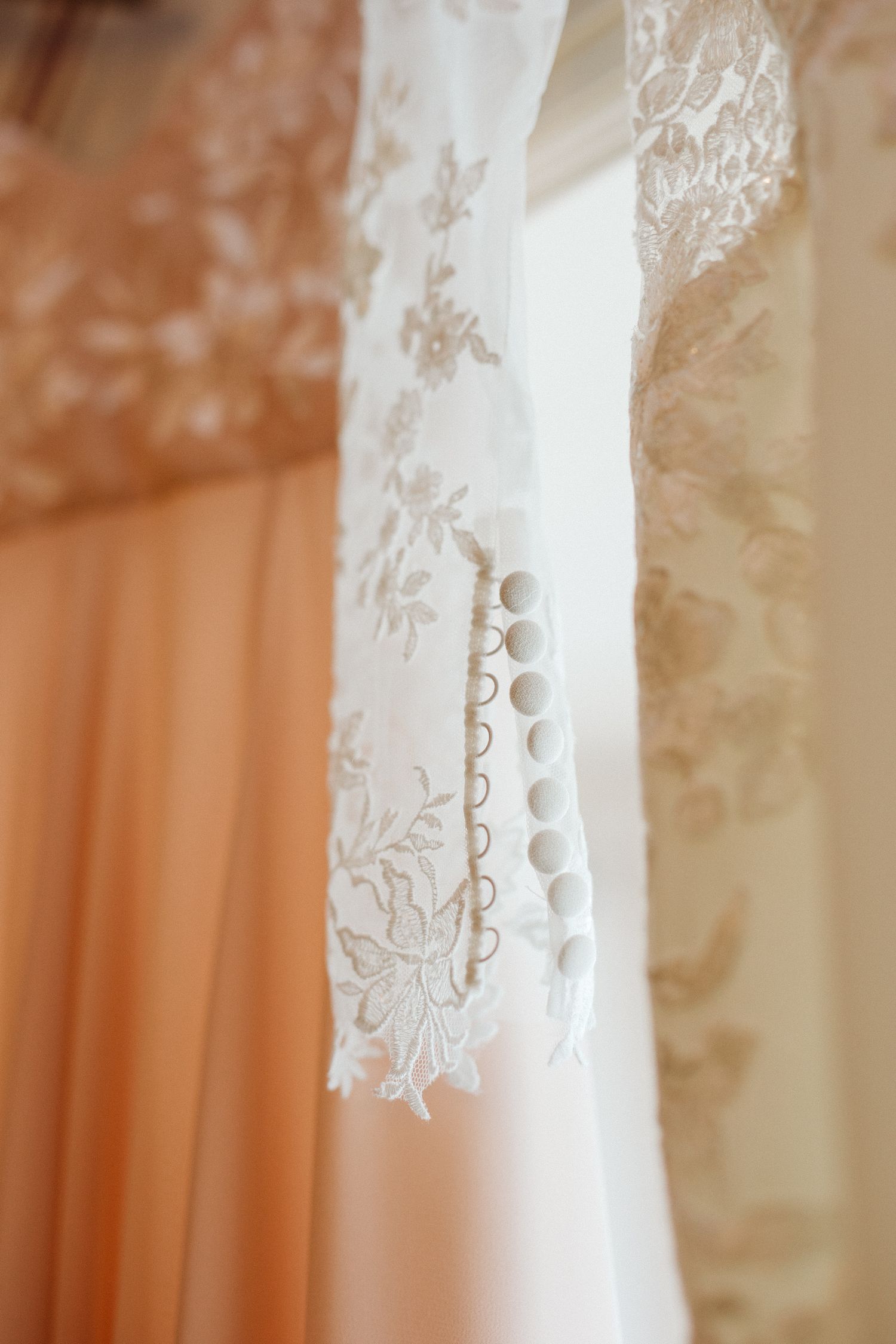 Detail shot of intricate white lace pattern on wedding dress fabric against a peach background.