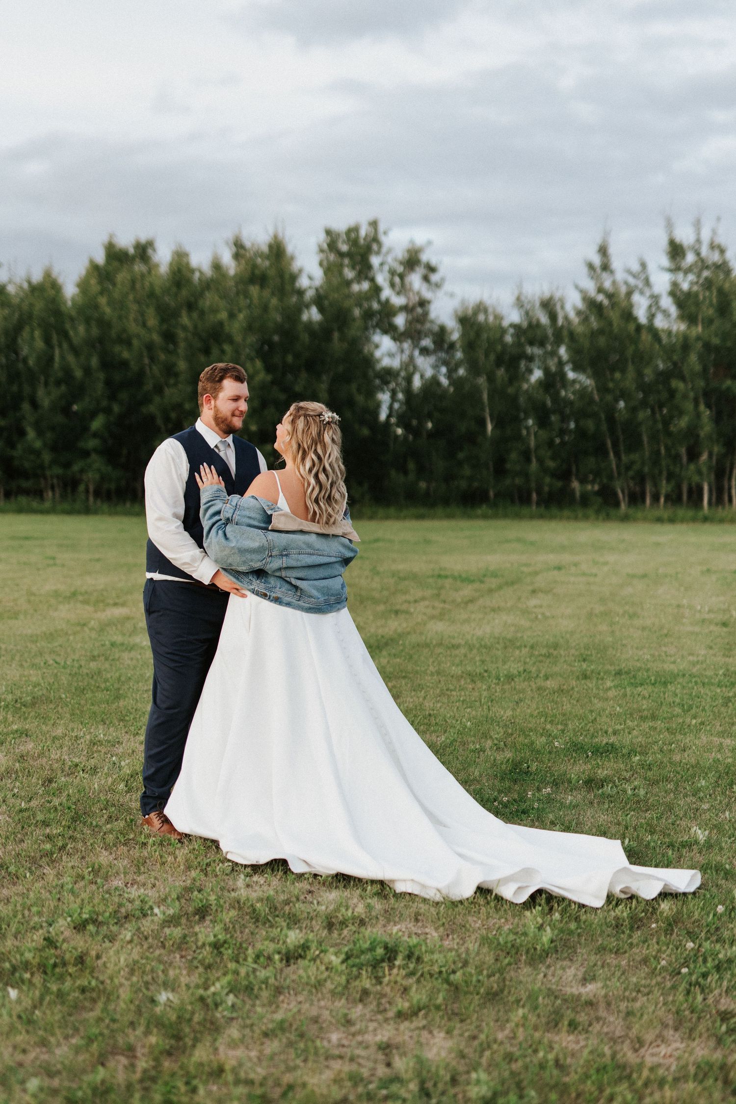 Romantic couple poses in grassy field with flowing white wedding dress.