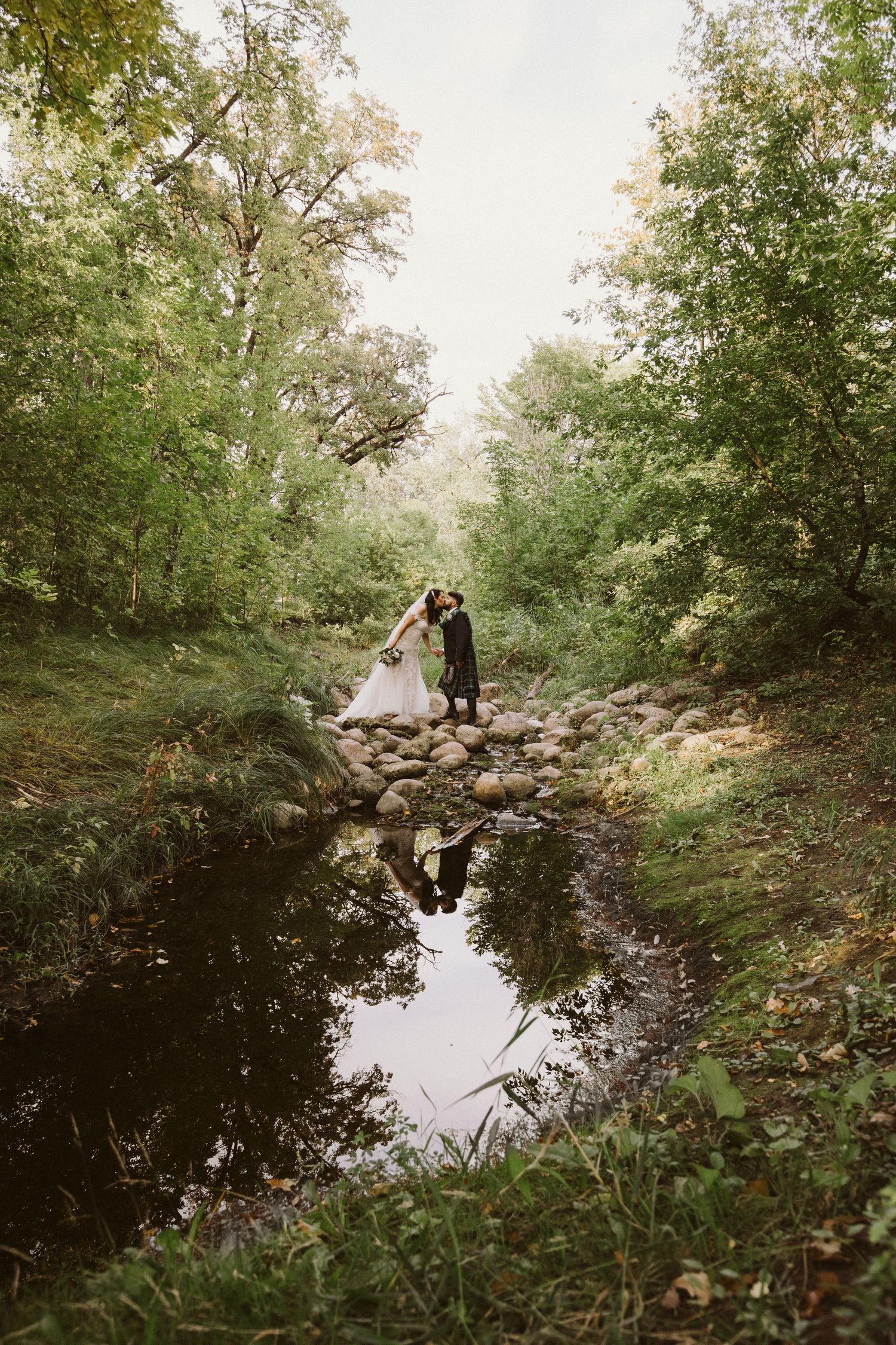 Tranquil stream in wooded area with rocks and reflection in the water.