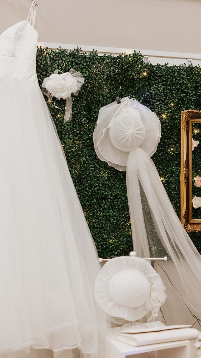 White wedding veils and bridal accessories displayed against a green hedge backdrop.
