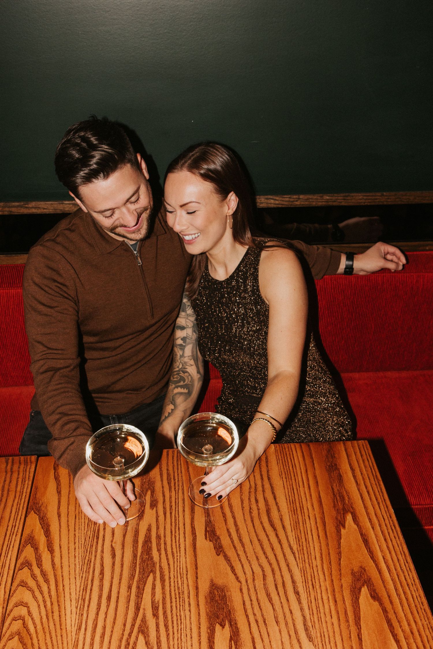 Intimate couple moment sharing drinks at wooden table in dark restaurant setting.