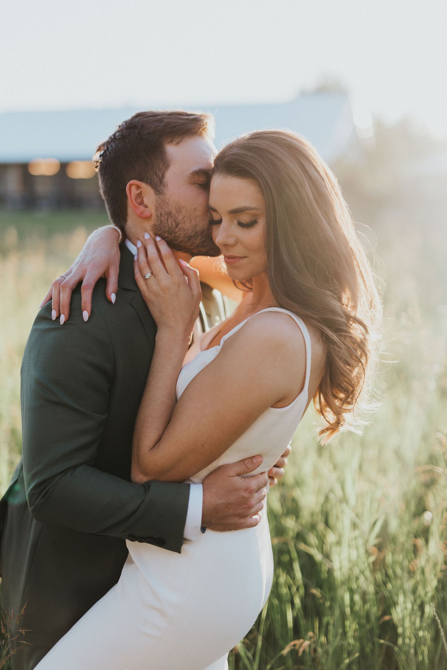 A romantic embrace in a sunlit field during a wedding photoshoot.