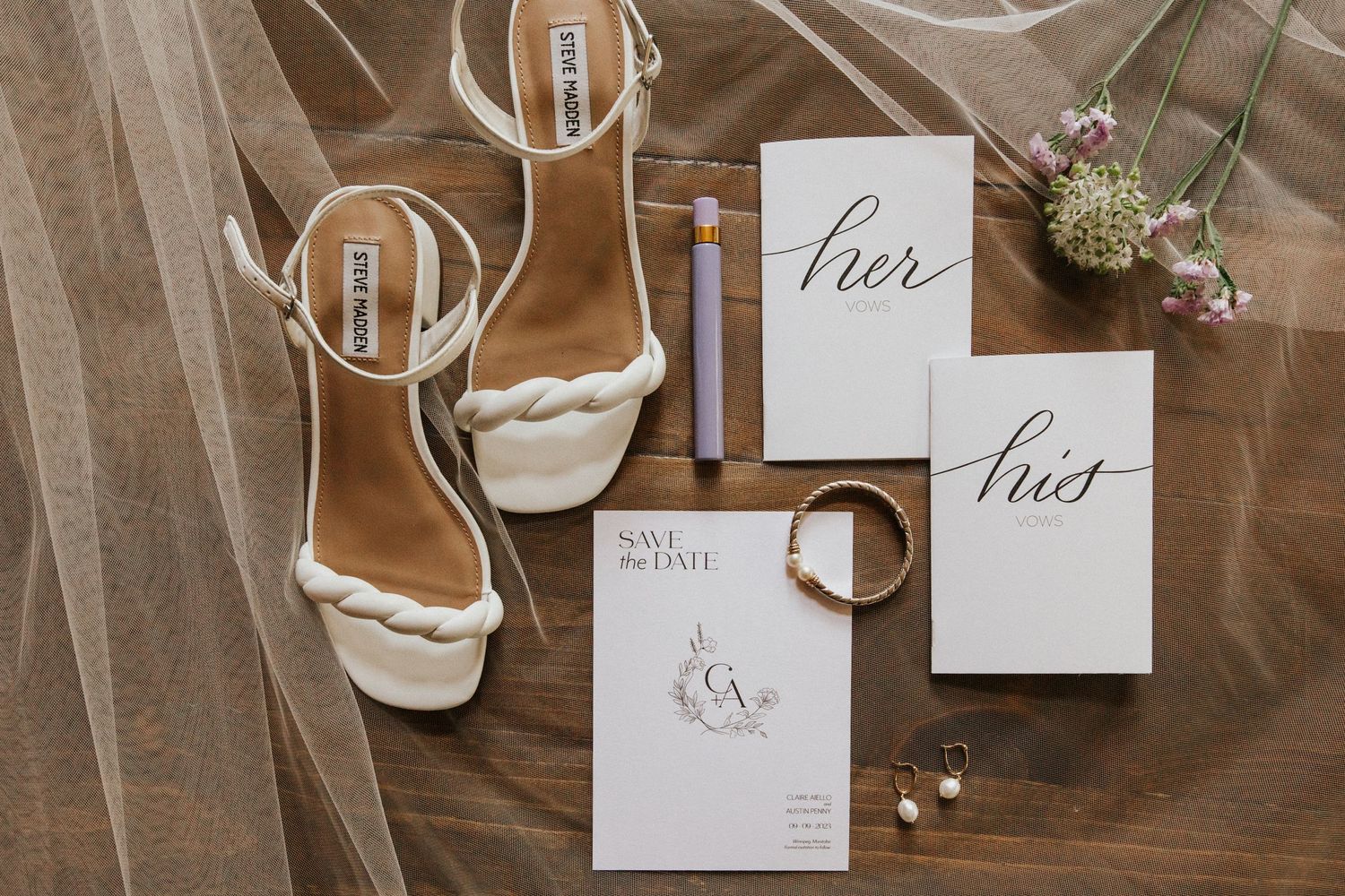 Wedding stationery and accessories flat lay with calligraphy invitations on wooden surface.