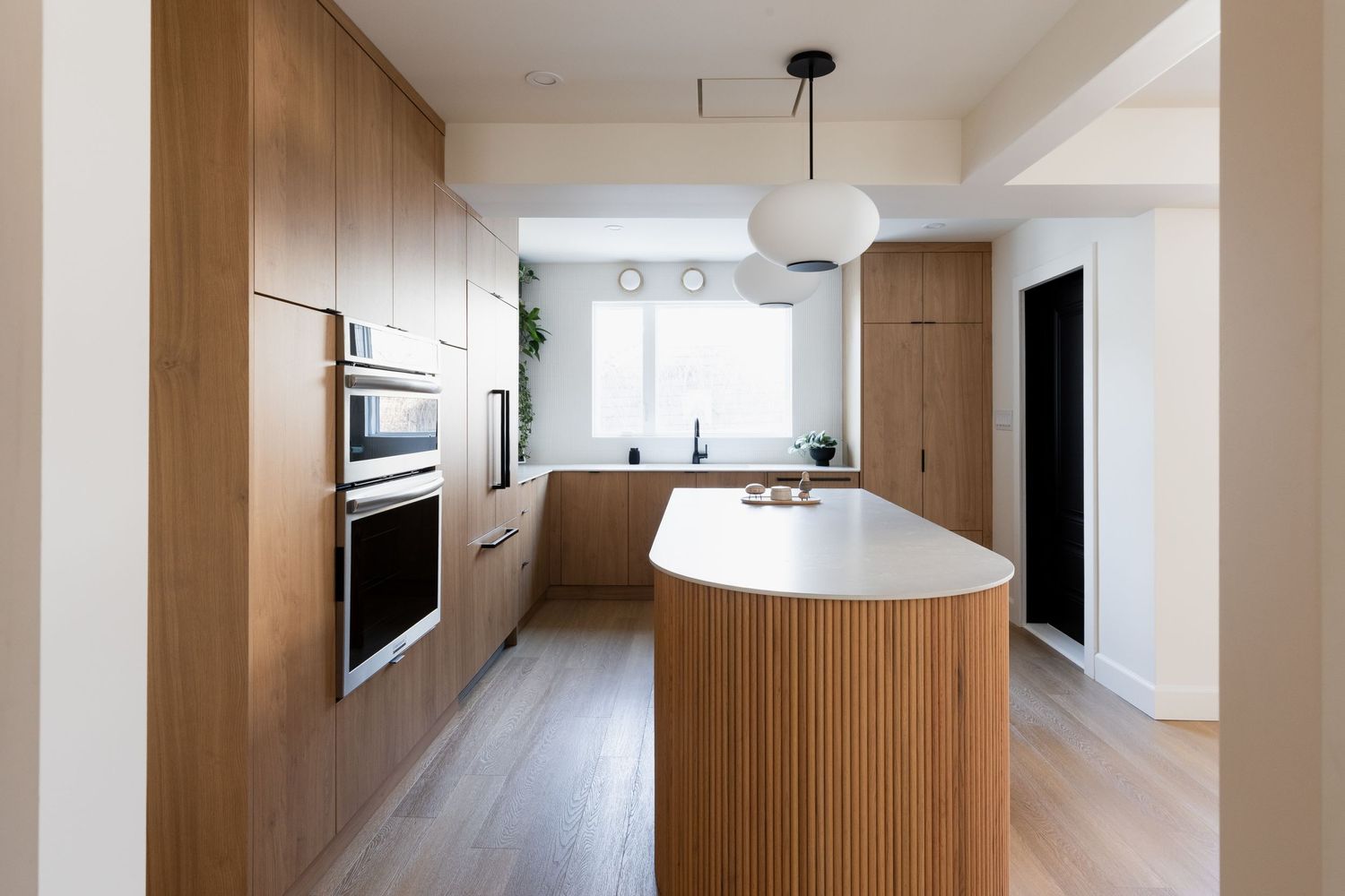 Minimalist white and wood kitchen with long hallway and pendant lighting creates a bright, airy atmosphere.