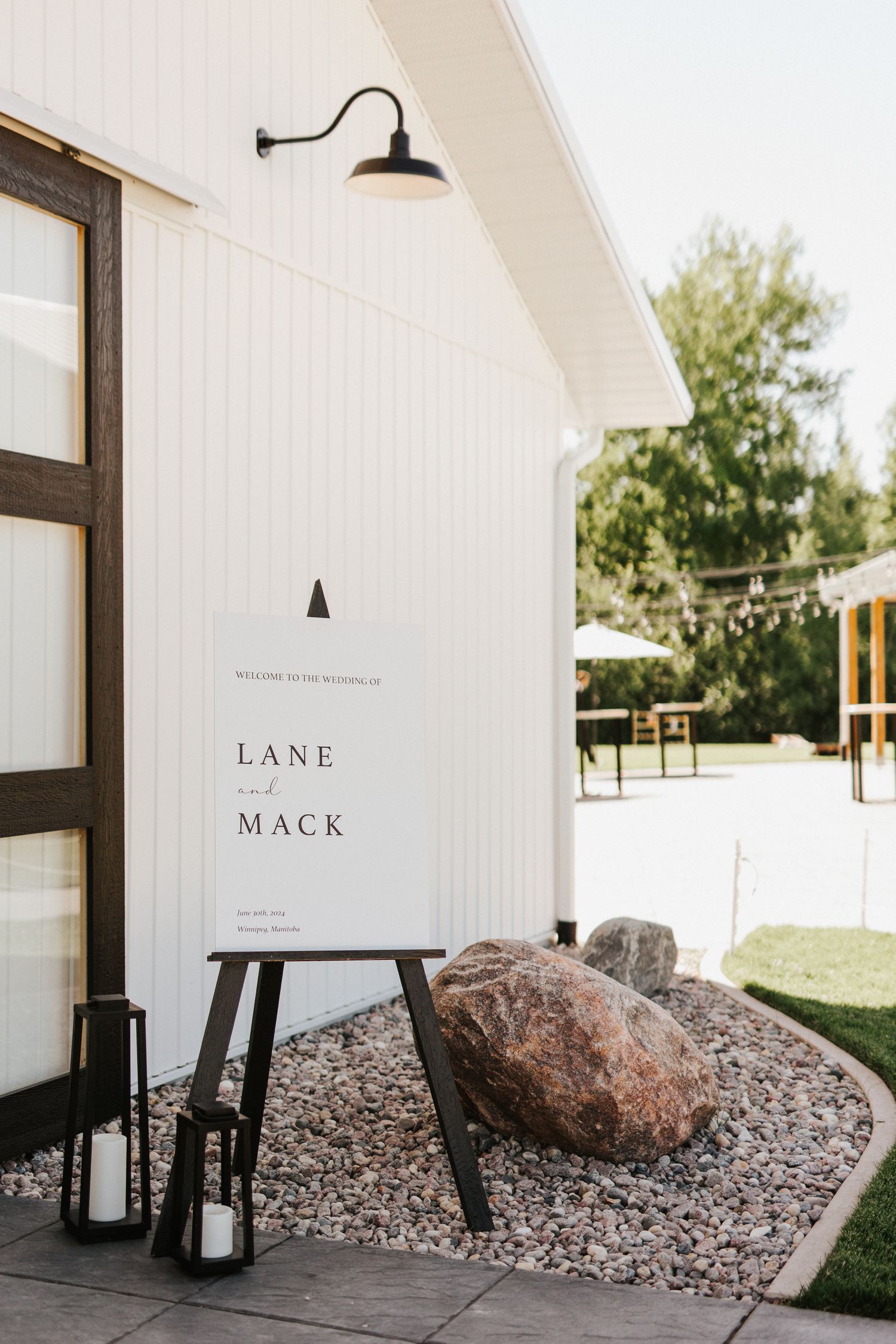 Modern white barn venue exterior with rustic stone landscaping and black accents.