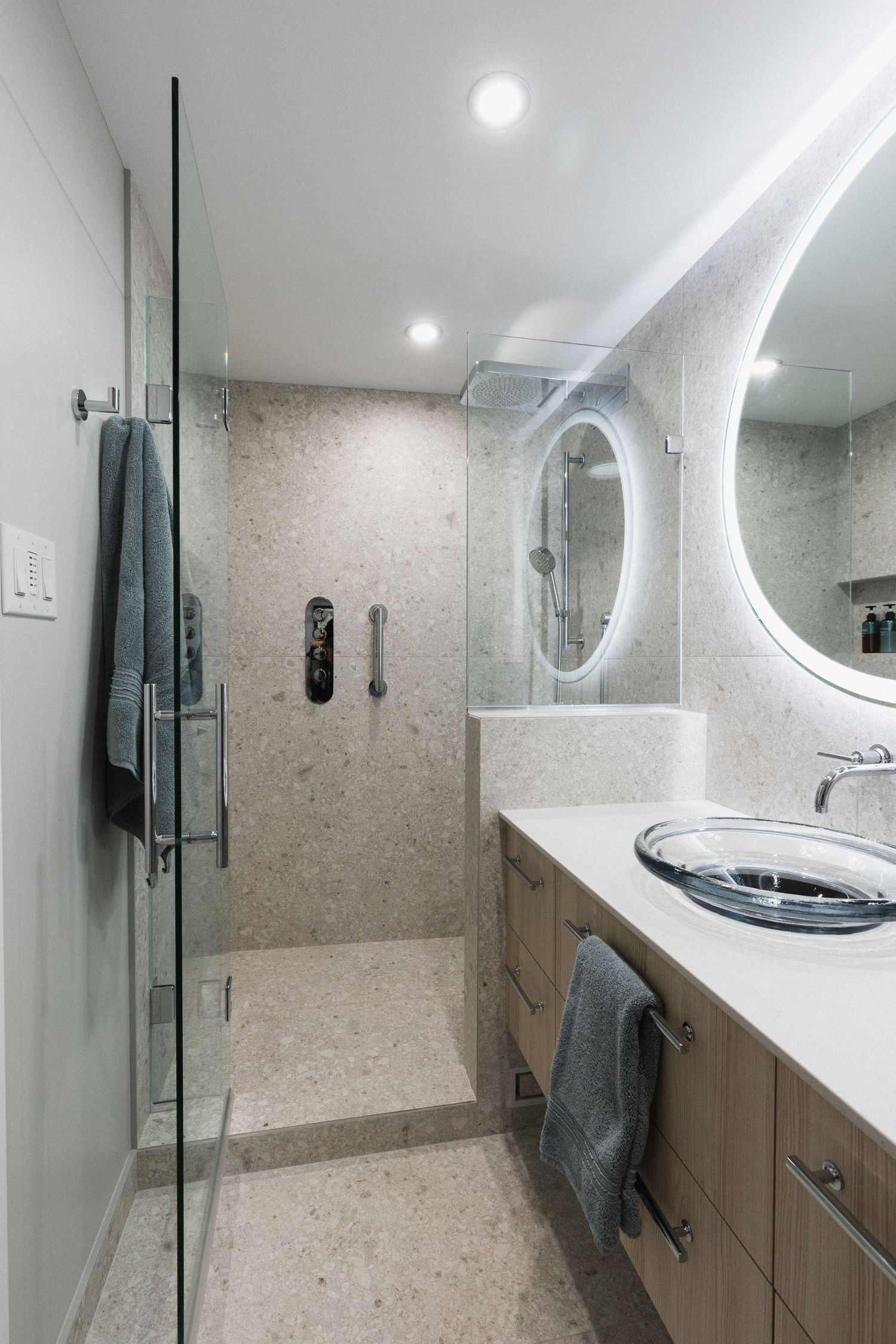 Modern bathroom featuring white countertops, built-in storage, and a backlit circular mirror.