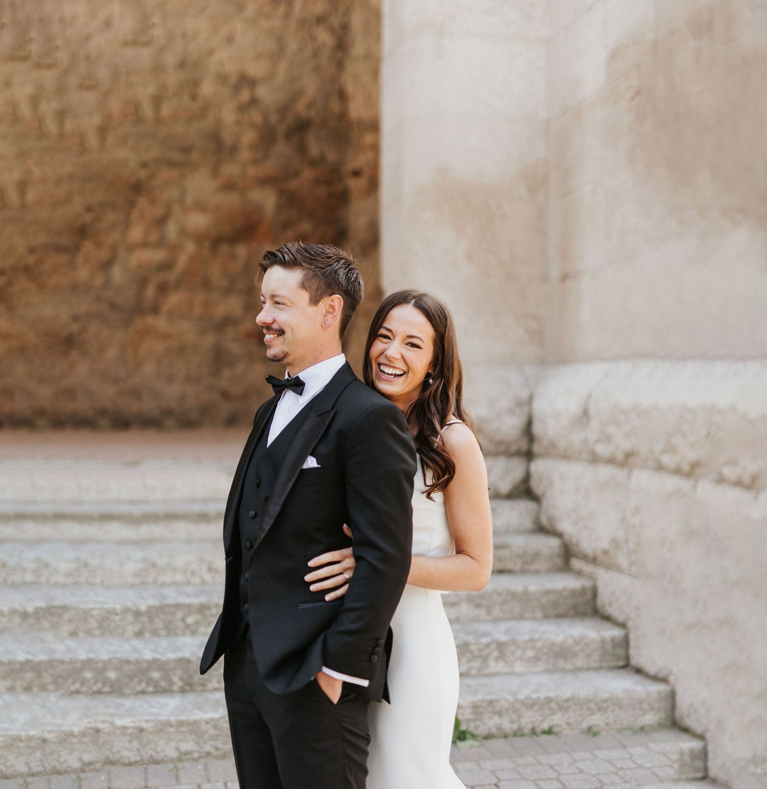 Joyful wedding couple sharing a candid moment on stone steps.