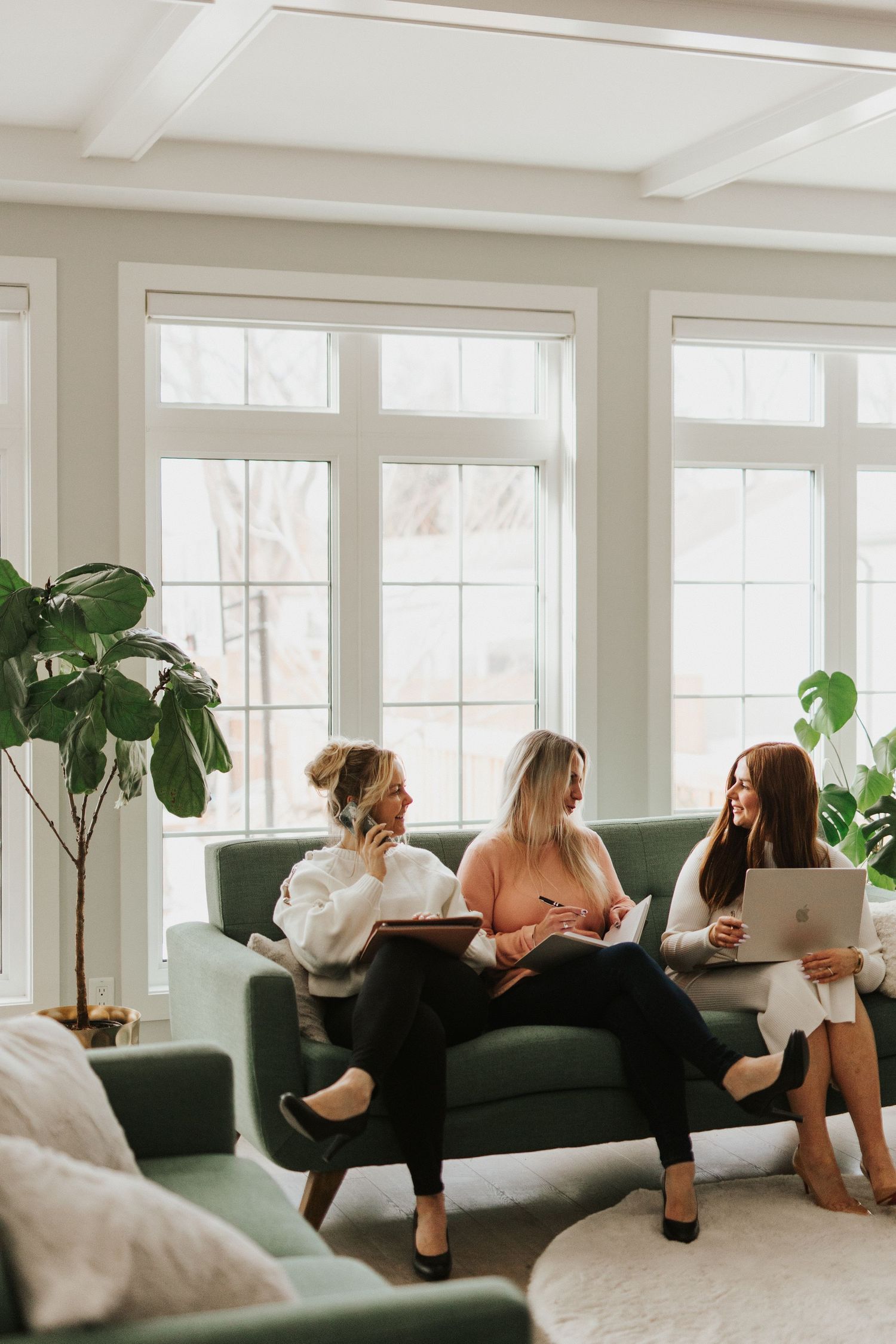 Business team lounging on green couch during casual meeting in bright sunlit room.