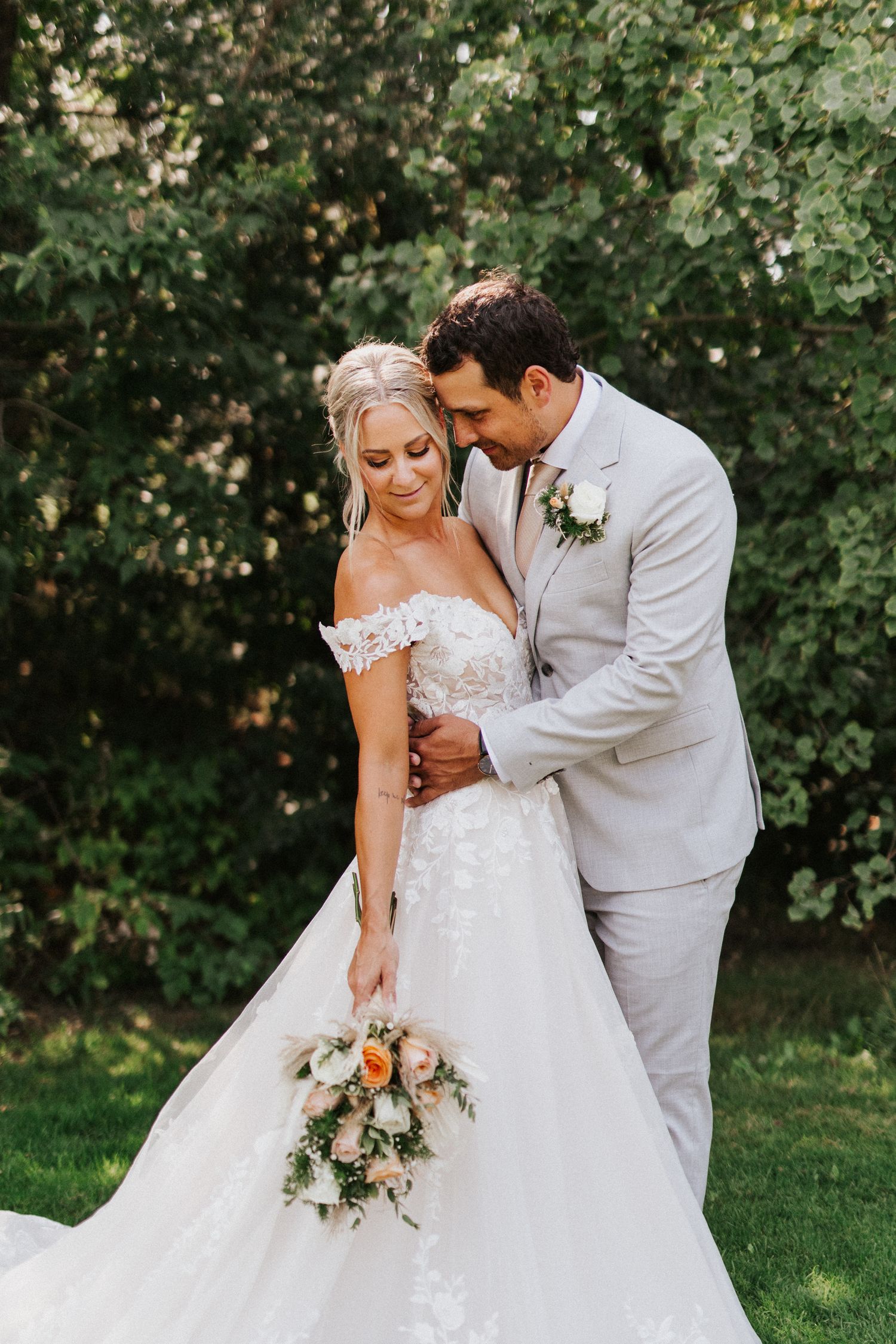 Romantic outdoor wedding photo with a flowing white gown and soft bouquet on a grassy lawn.