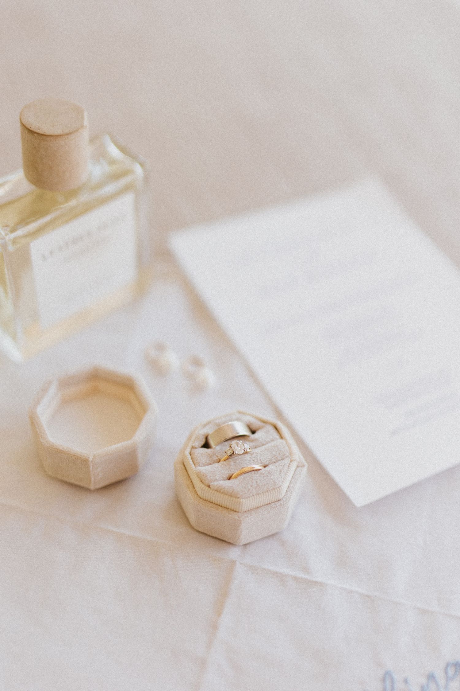 Minimalist wedding details with white stationery and hexagonal ring box on light linen.