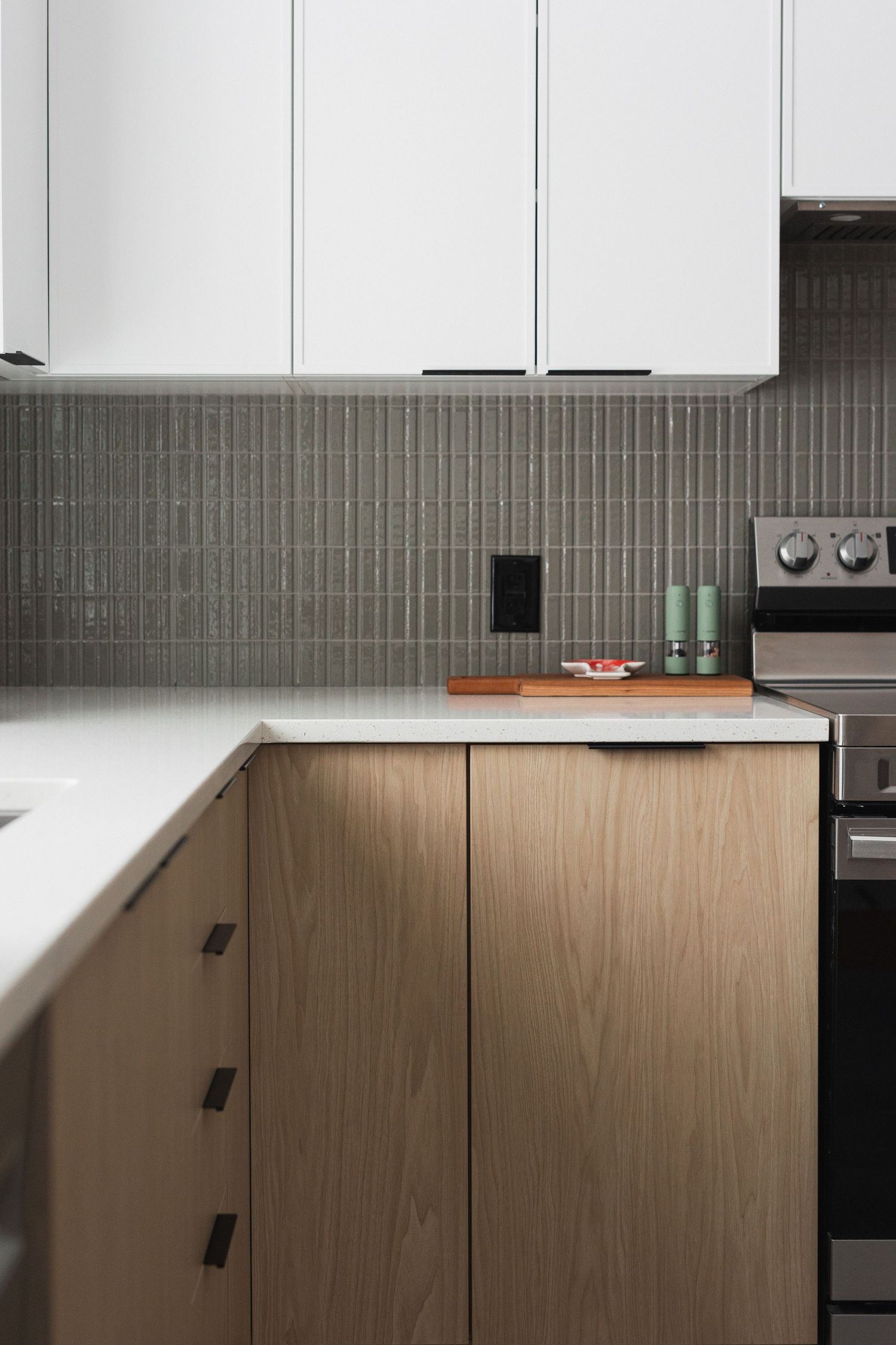 Contemporary kitchen design with white upper cabinets and wood lower cabinets against a green tiled backsplash.