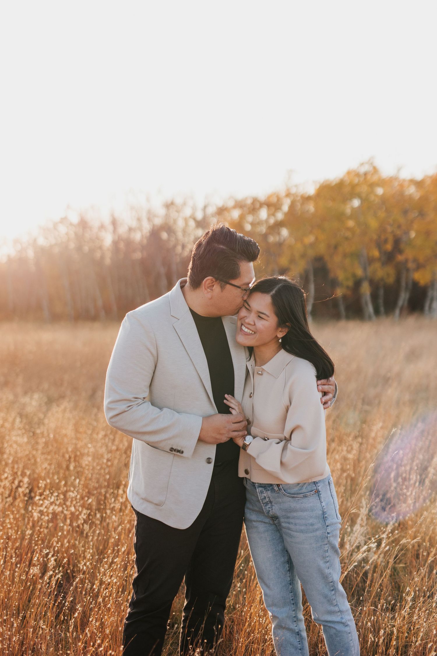 Affectionate couple embracing in field with autumn foliage backdrop.