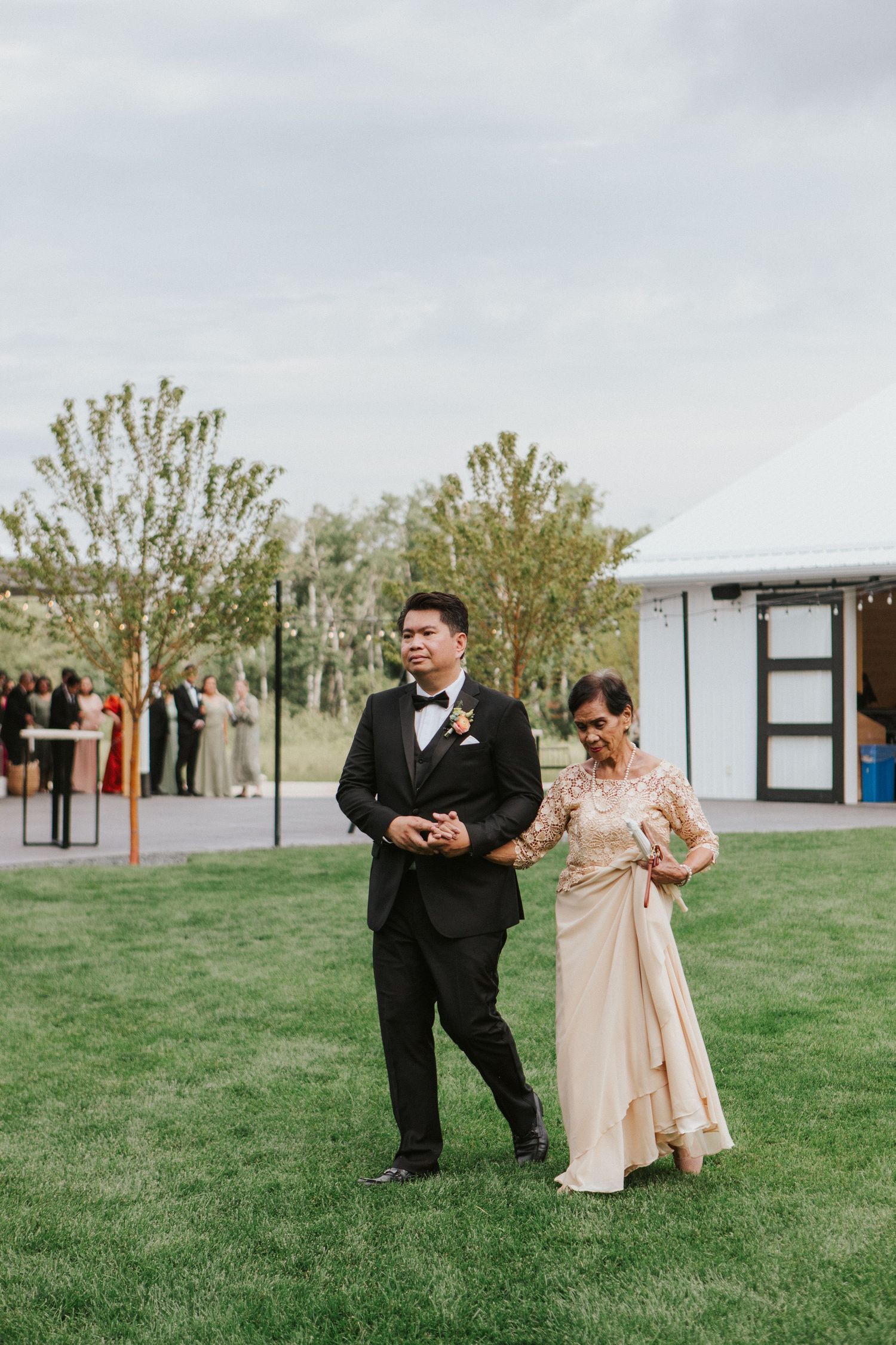 Wedding party members pose playfully on a grassy field with buildings in the background.
