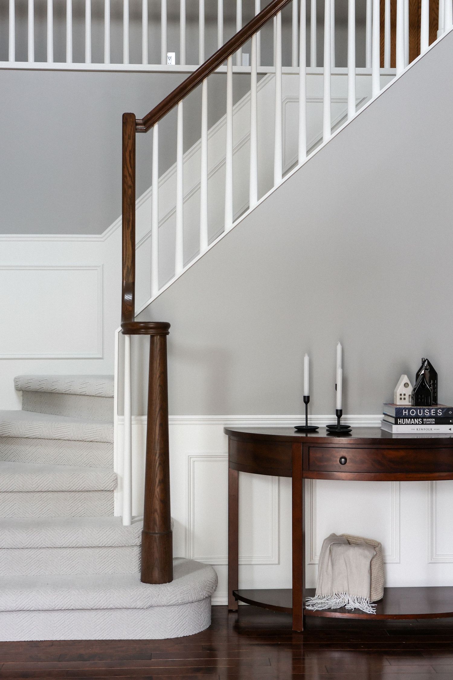 White staircase with dark wood handrail and minimalist entryway decor.