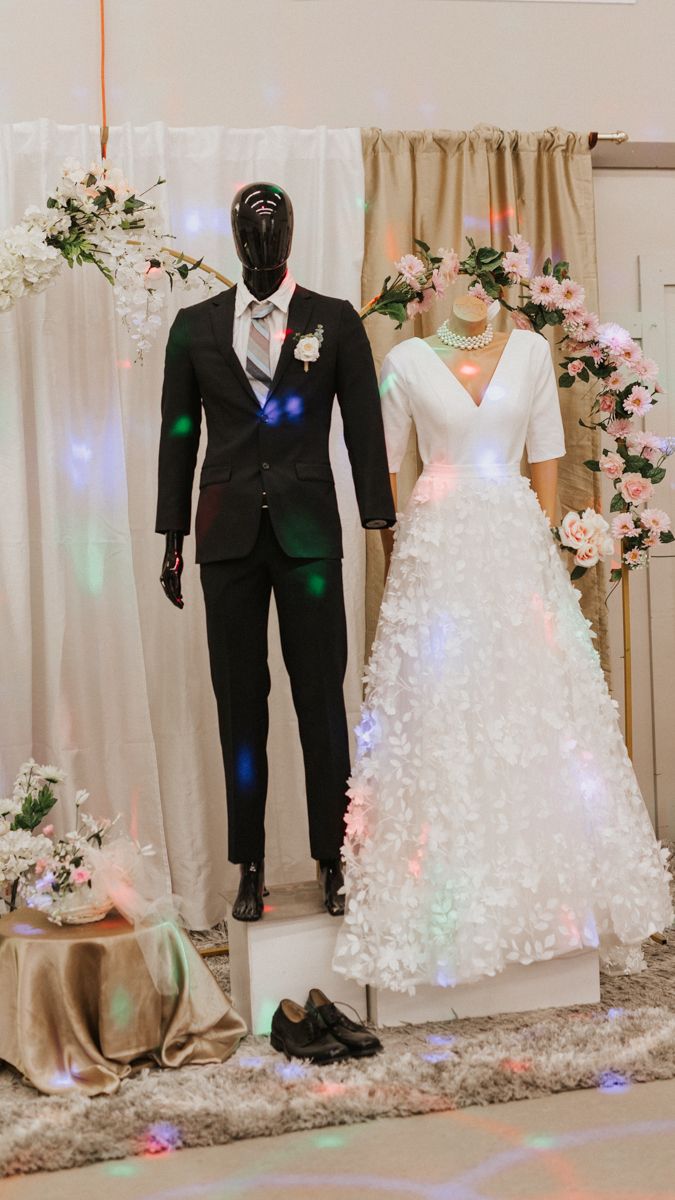 Wedding attire display featuring illuminated white gown and formal suits with decorative lighting.