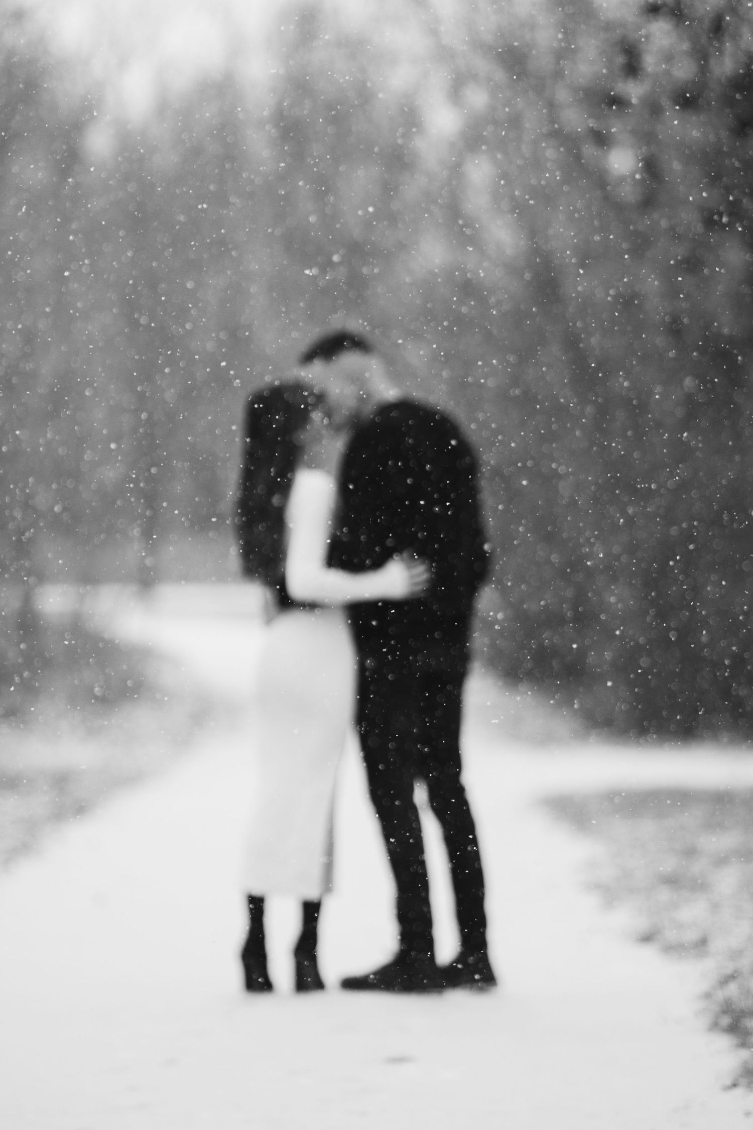 Silhouettes of a couple embrace in a snowy winter scene with snowflakes falling around them.